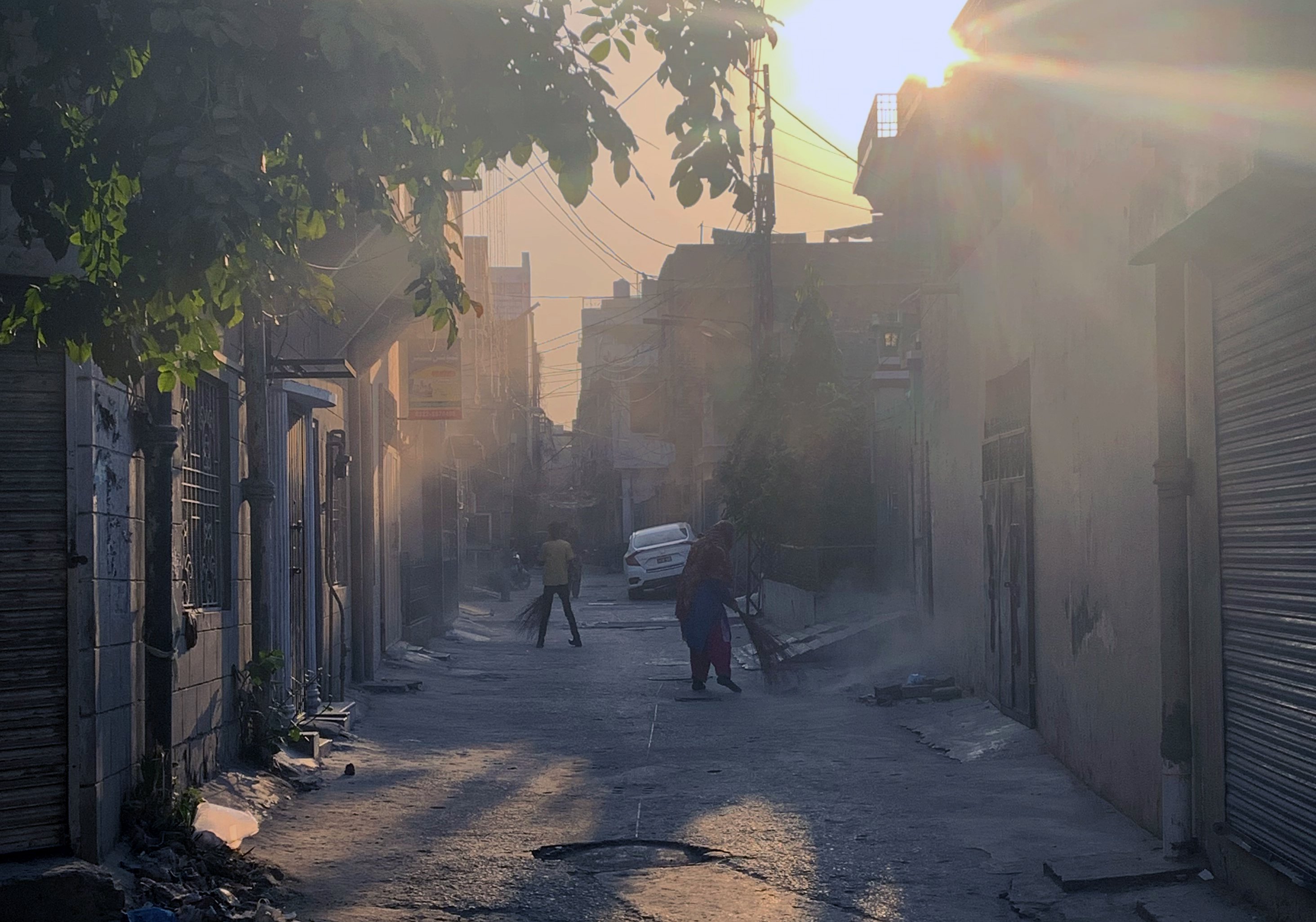 A photo of a street in the middle of houses with two people sweeping.