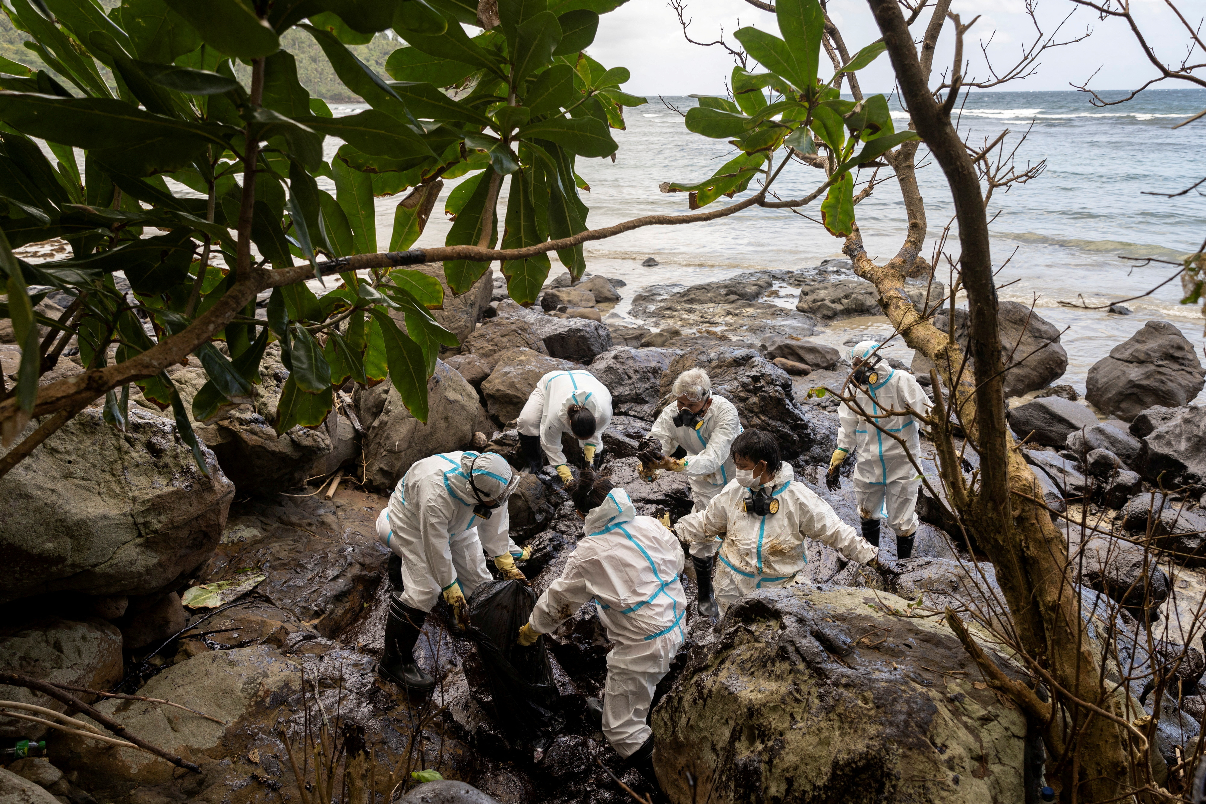 Volunteers in personal protective equipment clean up the oil spill