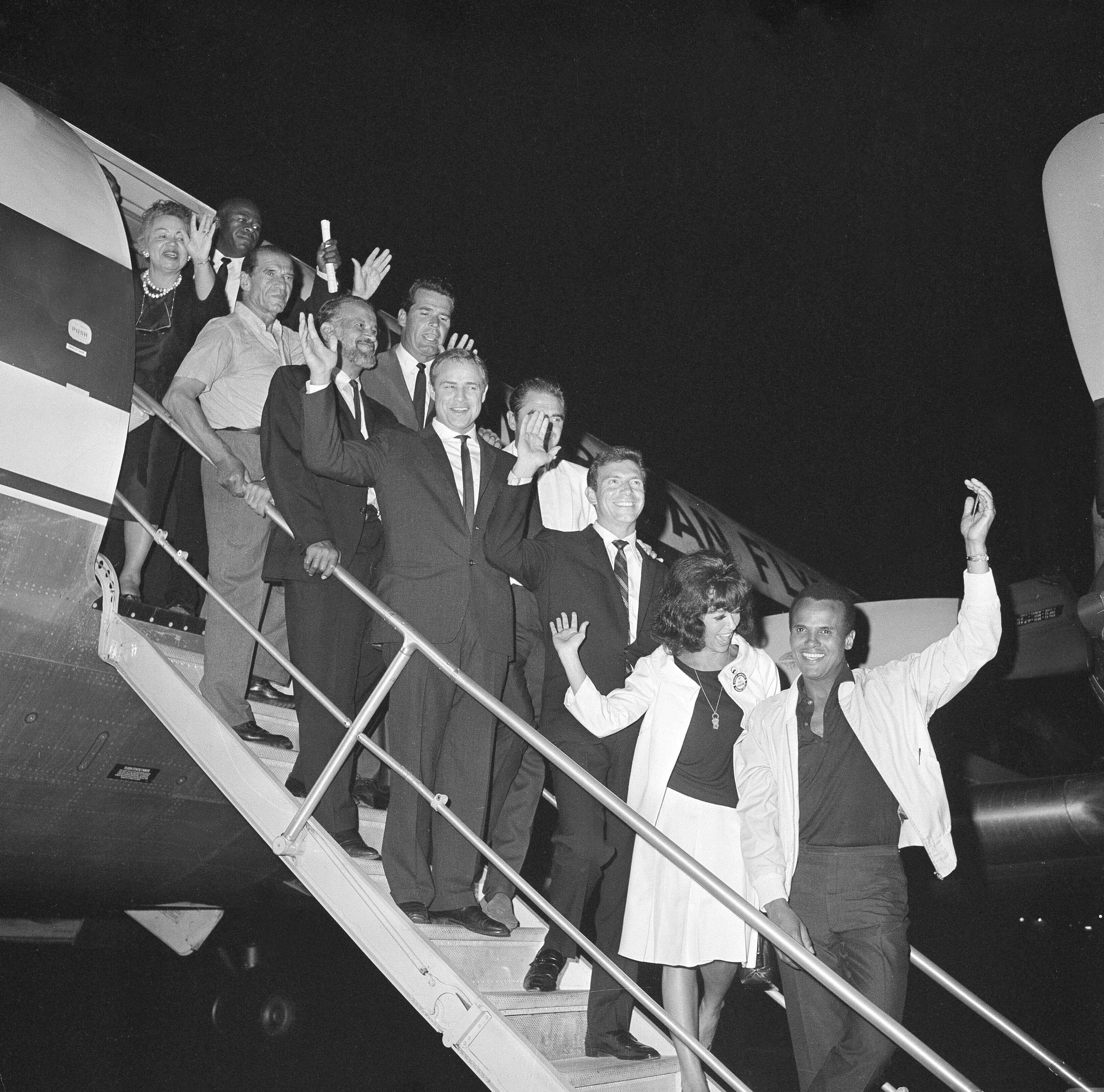 Hollywood celebrities pose on the steps of a plane in 1963