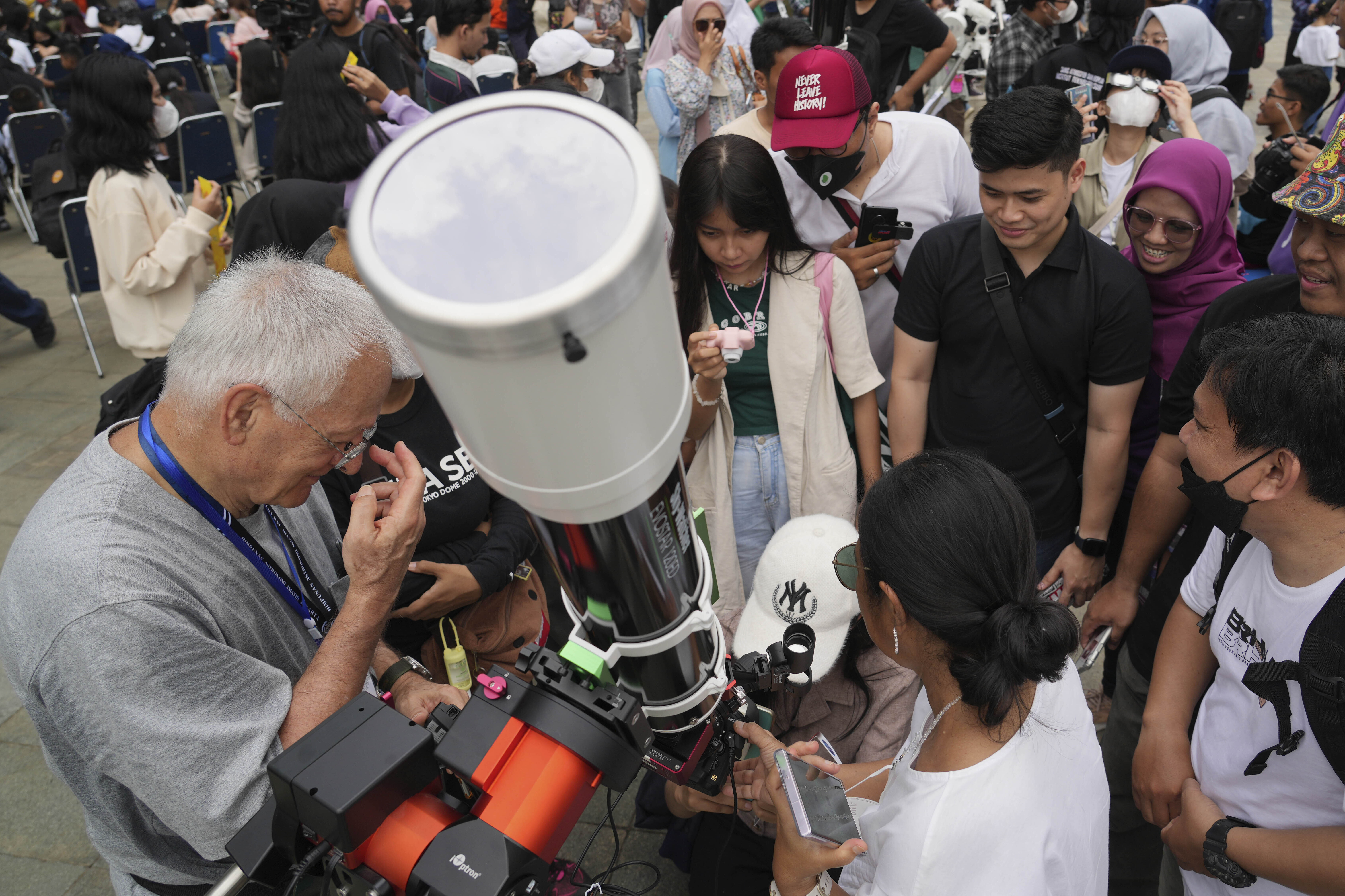 People gathered around a large telescope in Jakarta as they take turns to view the partial solar eclipse, Some are children.