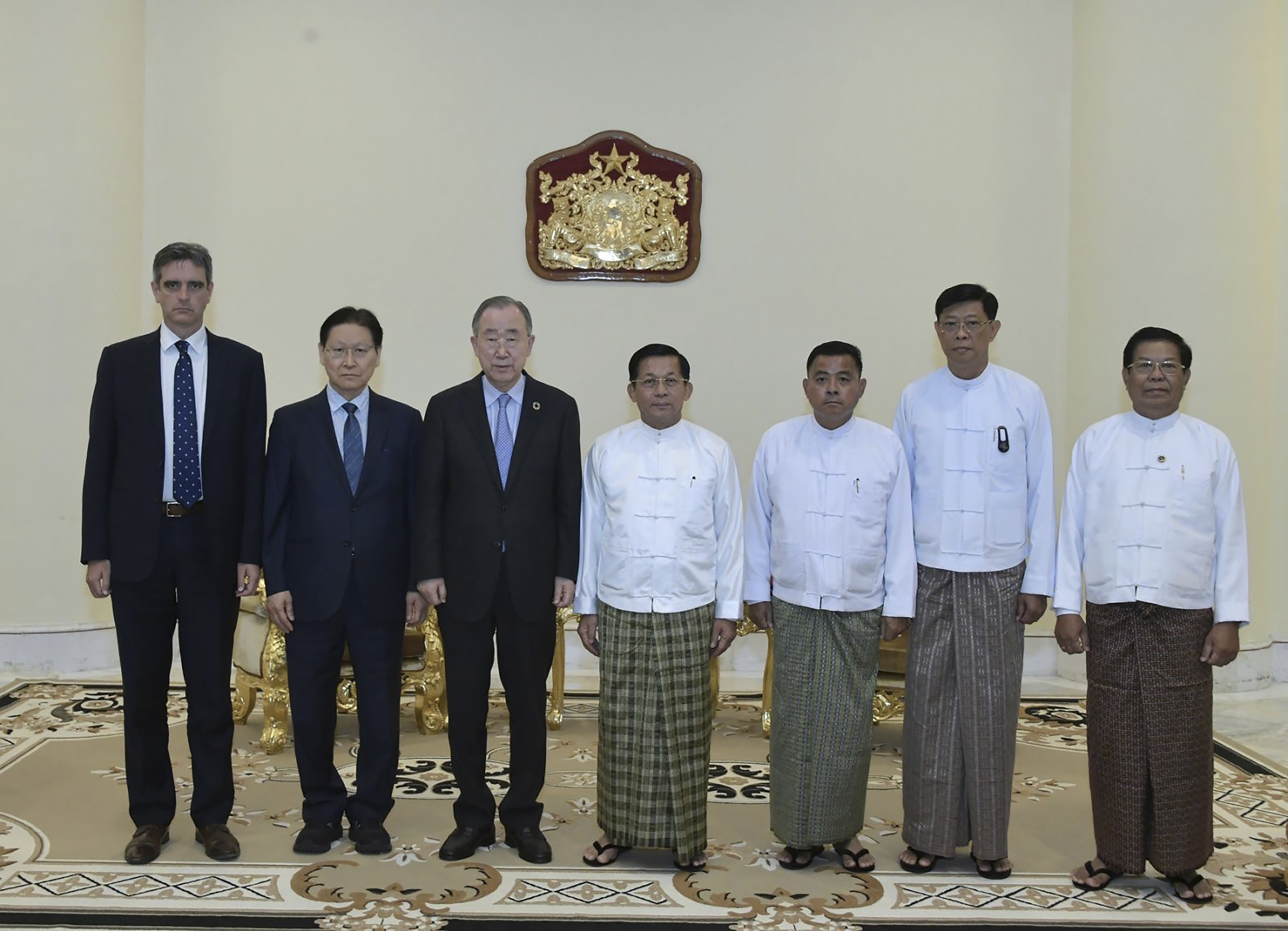 Former UN chief Ban Ki-moon and Senior General Min Aung Hlaing stand with their officials following their meeting in Naypyidaw. Ban and his two officials are in suits on the left. Min Aung Hlaing and his three officials in traditional Burmese dress on the right. It's a formal photograph.