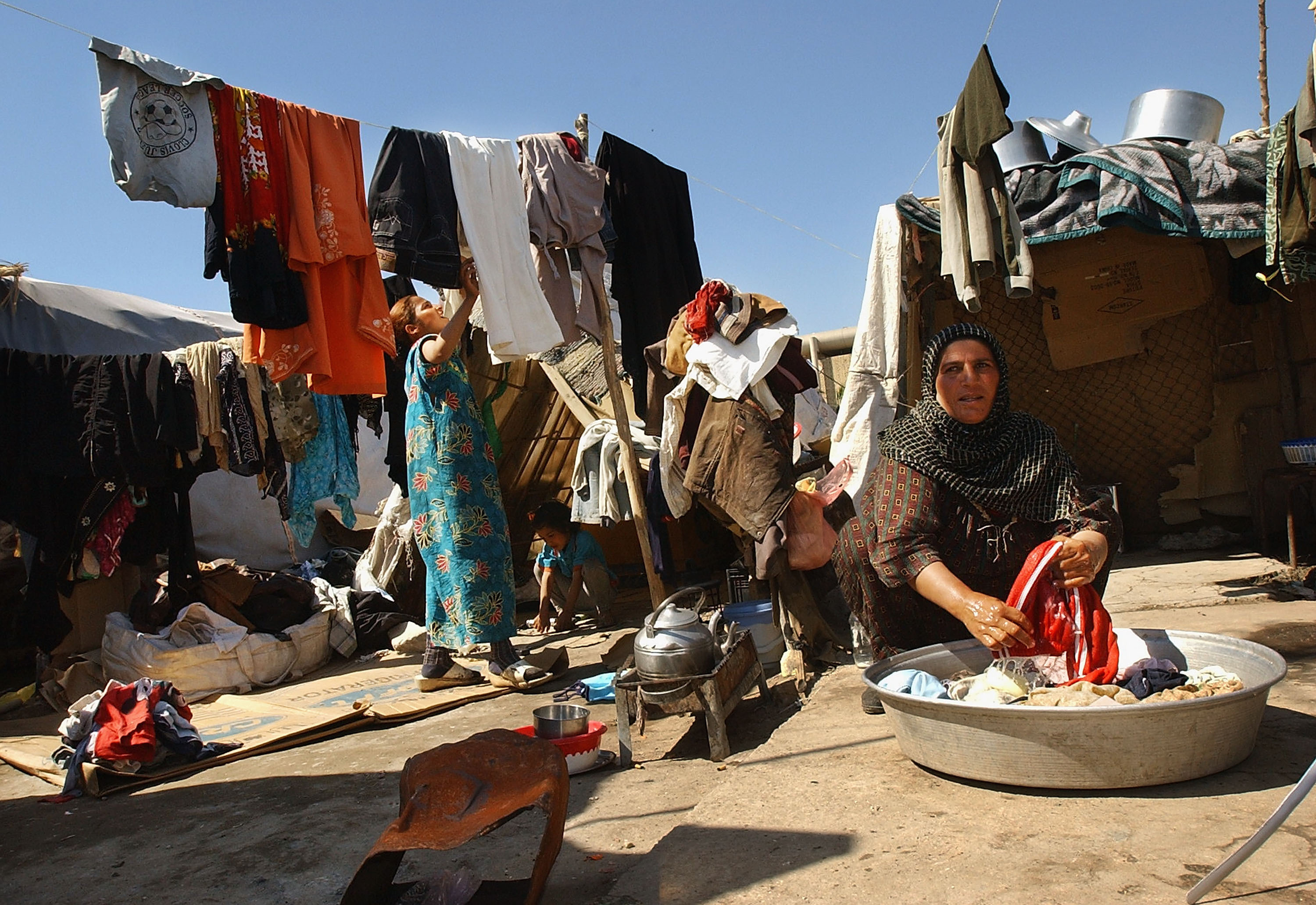 BAGHDAD, IRAQ - MARCH 20: Firyal Ashoor washes clothes in front of a tent that she and her ten member family live in after they were kicked out of their house because they could not afford the rent after the fall of Baghdad March 20, 2005 in the Karradh district of Baghdad, Iraq. Two years after the US-led invasion, Iraqis continue to suffer from a lack of electricity and a good system of sewage disposal as insurgent attacks continue against Iraqi security forces and general Iraqi infrastructure. (Photo by Wathiq Khuzaie/Getty Images)