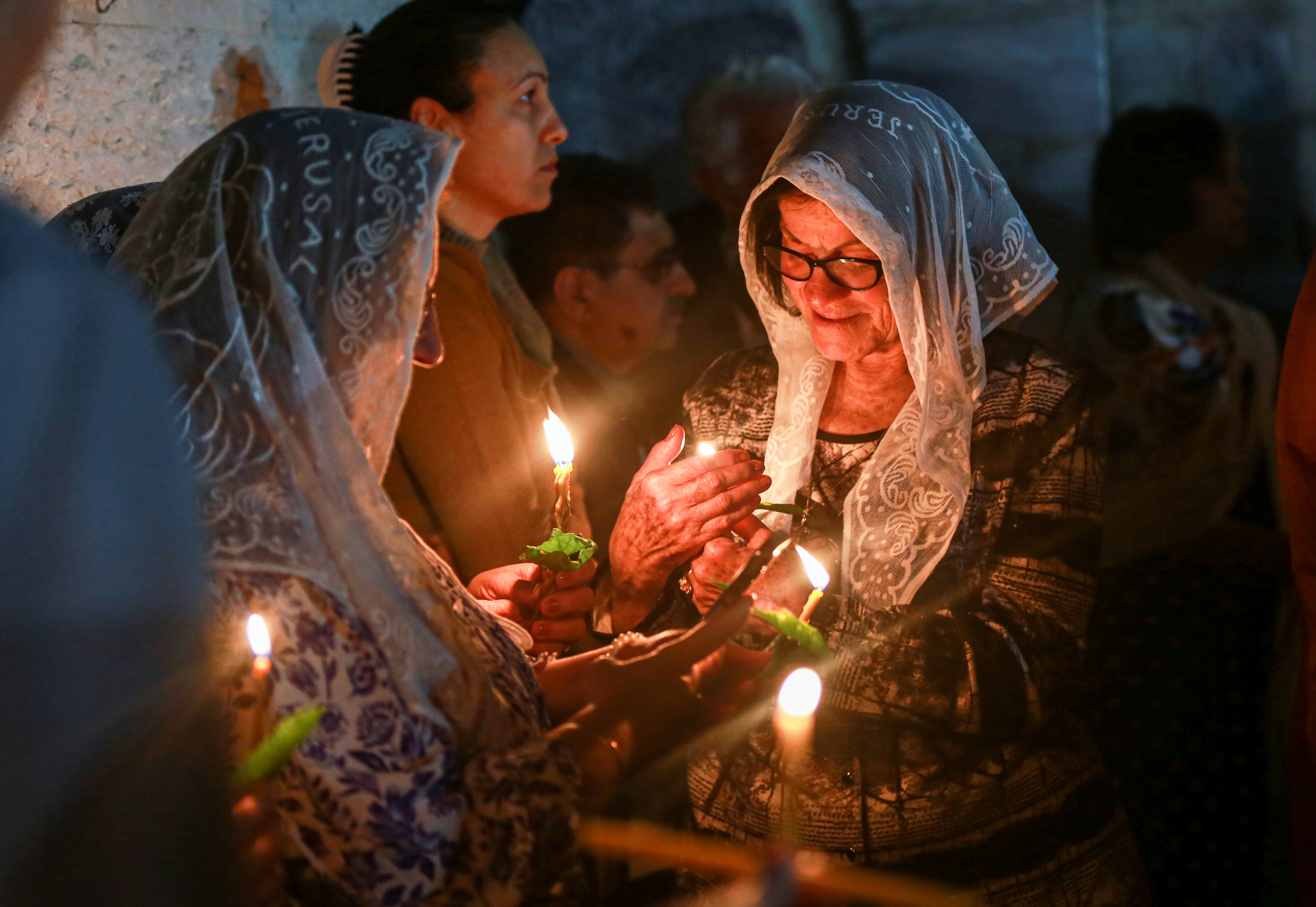Worshippers in the courtyard light their candles from each other