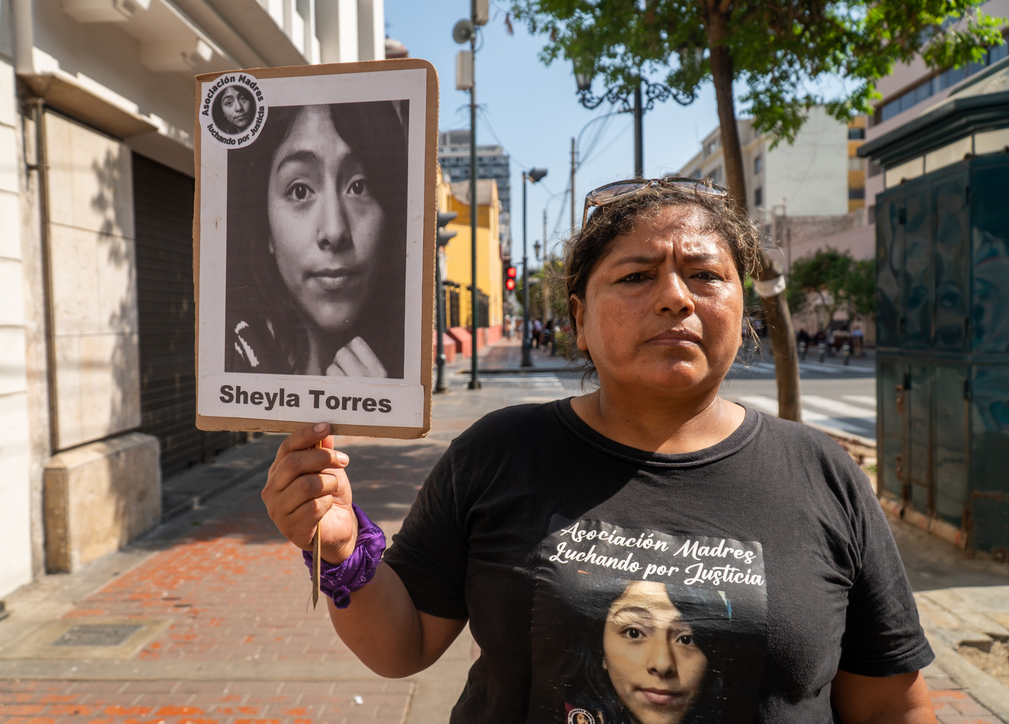 A woman walks down the street with a sign that features the name and portrait of Sheyla Torres. She is also wearing a t-shirt with Sheila's face on it.