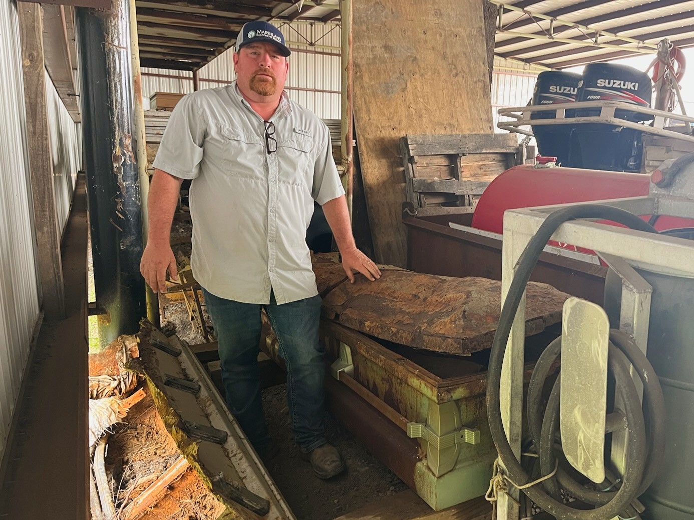 Hebert places his hand on a casket he recovered from the marshes by airboat, after it was displaced by Hurricane Laura in August 2020. He keeps the caskets in his workspace while waiting for the state to collect them