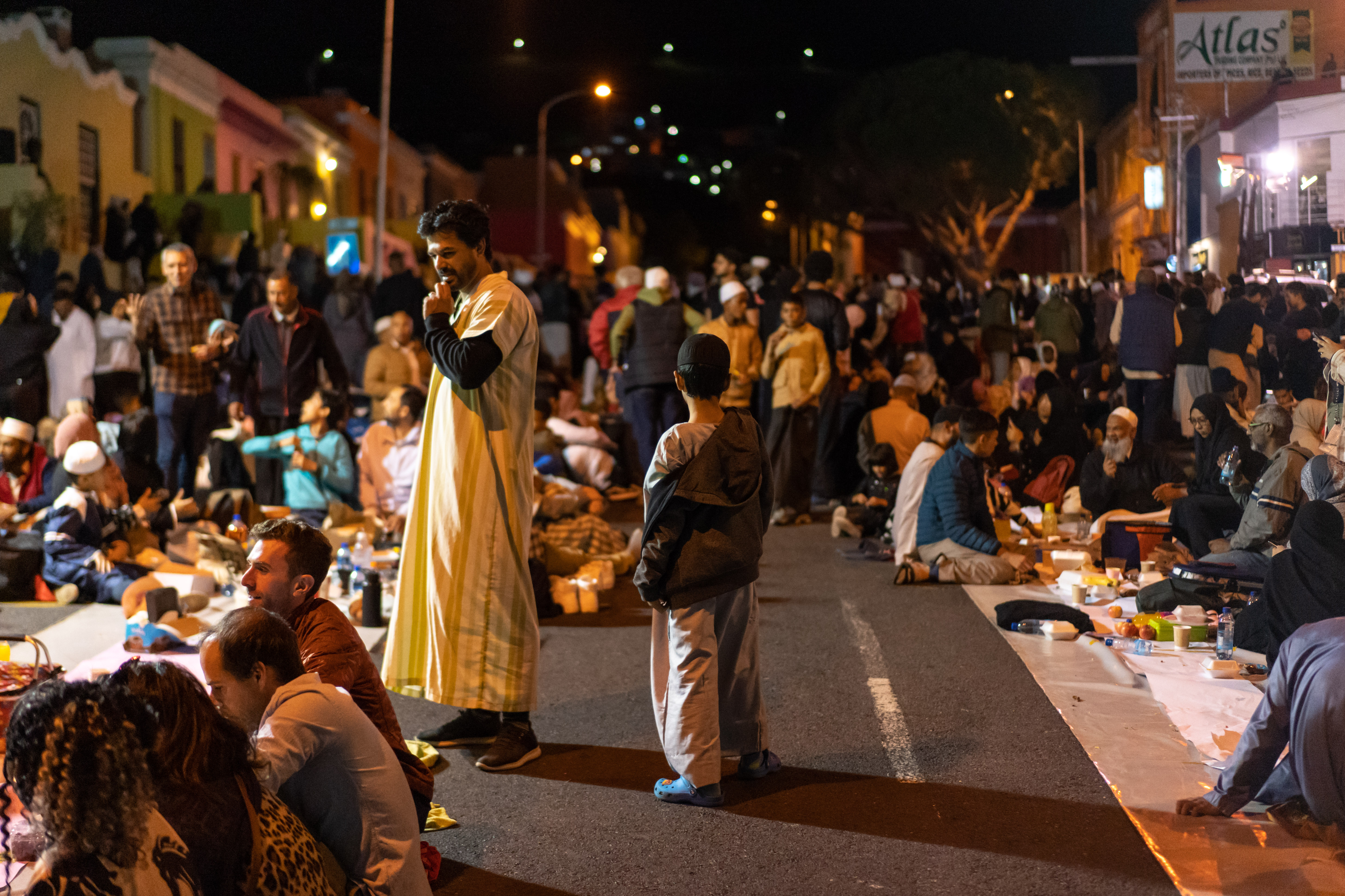 A photo of people sitting in the road eating on blankets and tables.