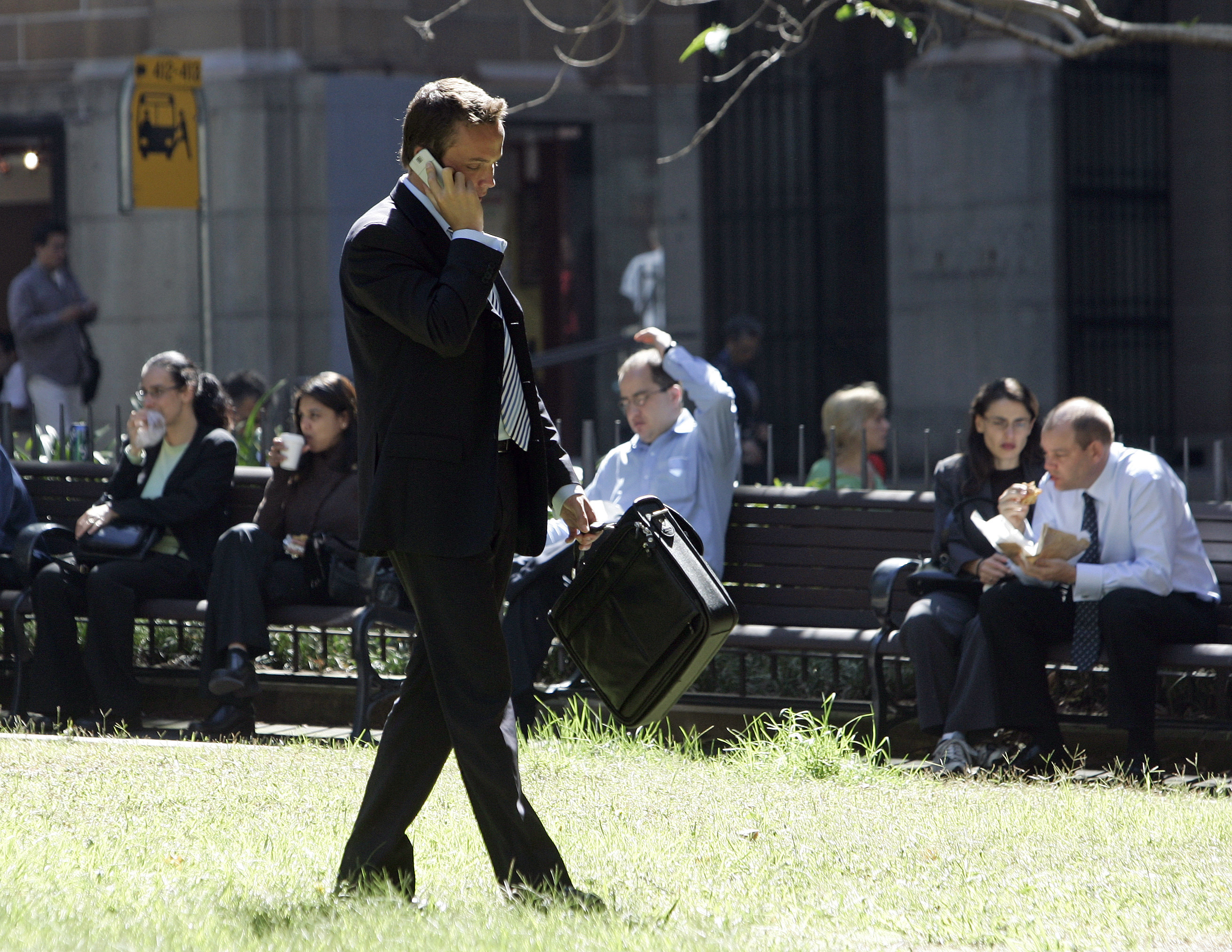 A businessman talks on his mobile phone as other office workers have lunch in a central Sydney park April 3, 2006