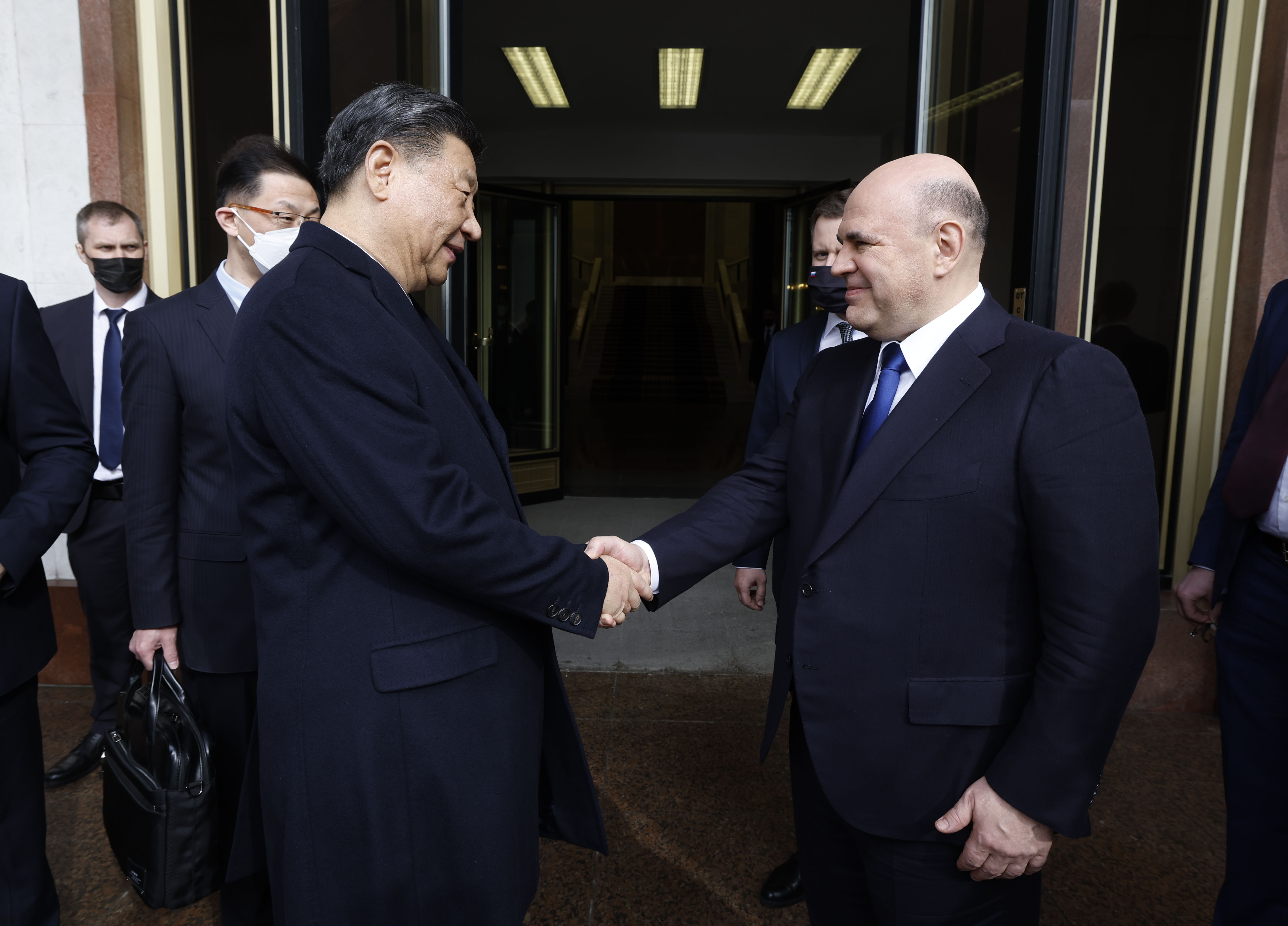 Russian Prime Minister Mikhail Mishustin smiling as he meets China's President Xi Jinping in Moscow. The two men are shaking hands.