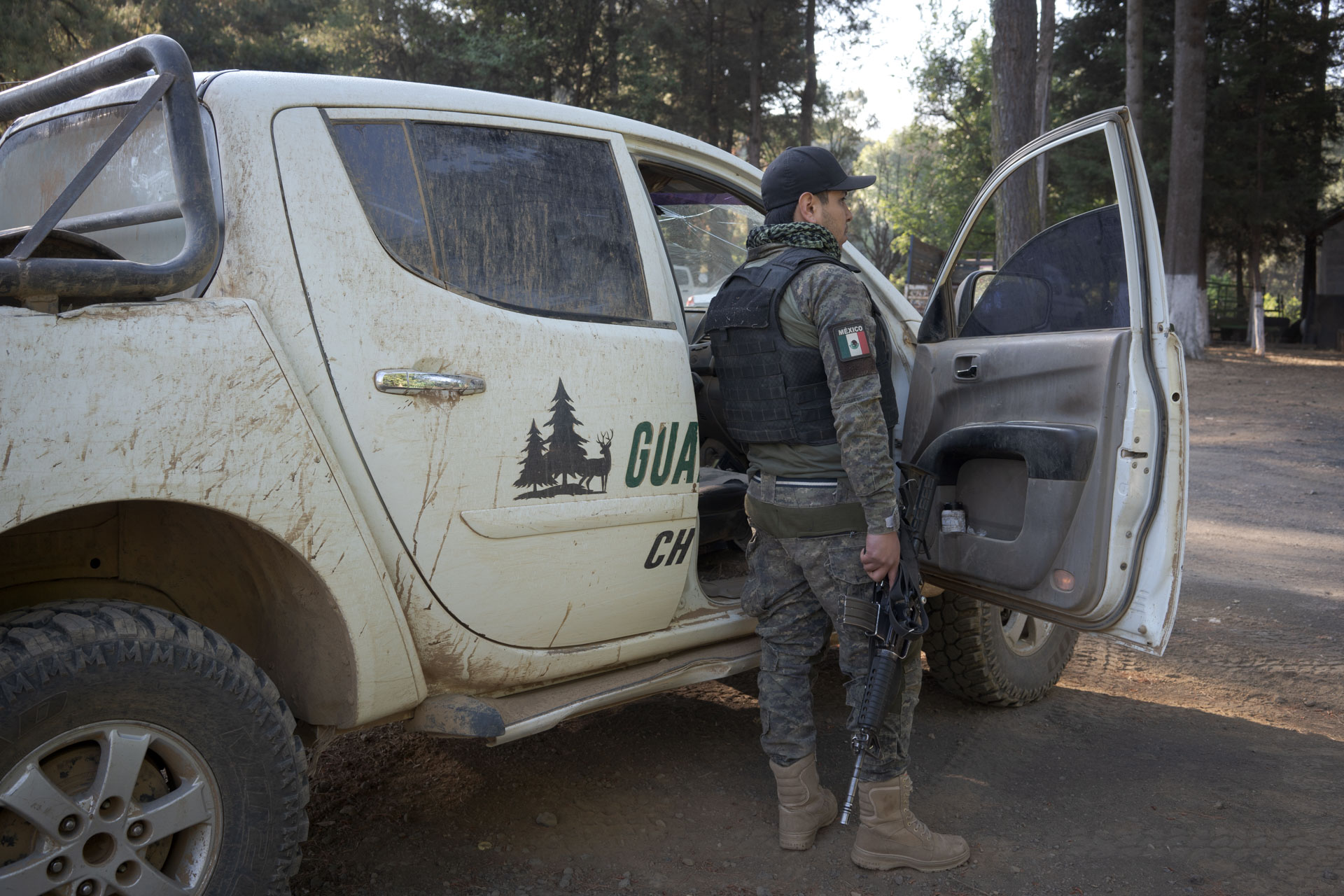 A man in military-style fatigues and a flak jacket stands outside a white truck.