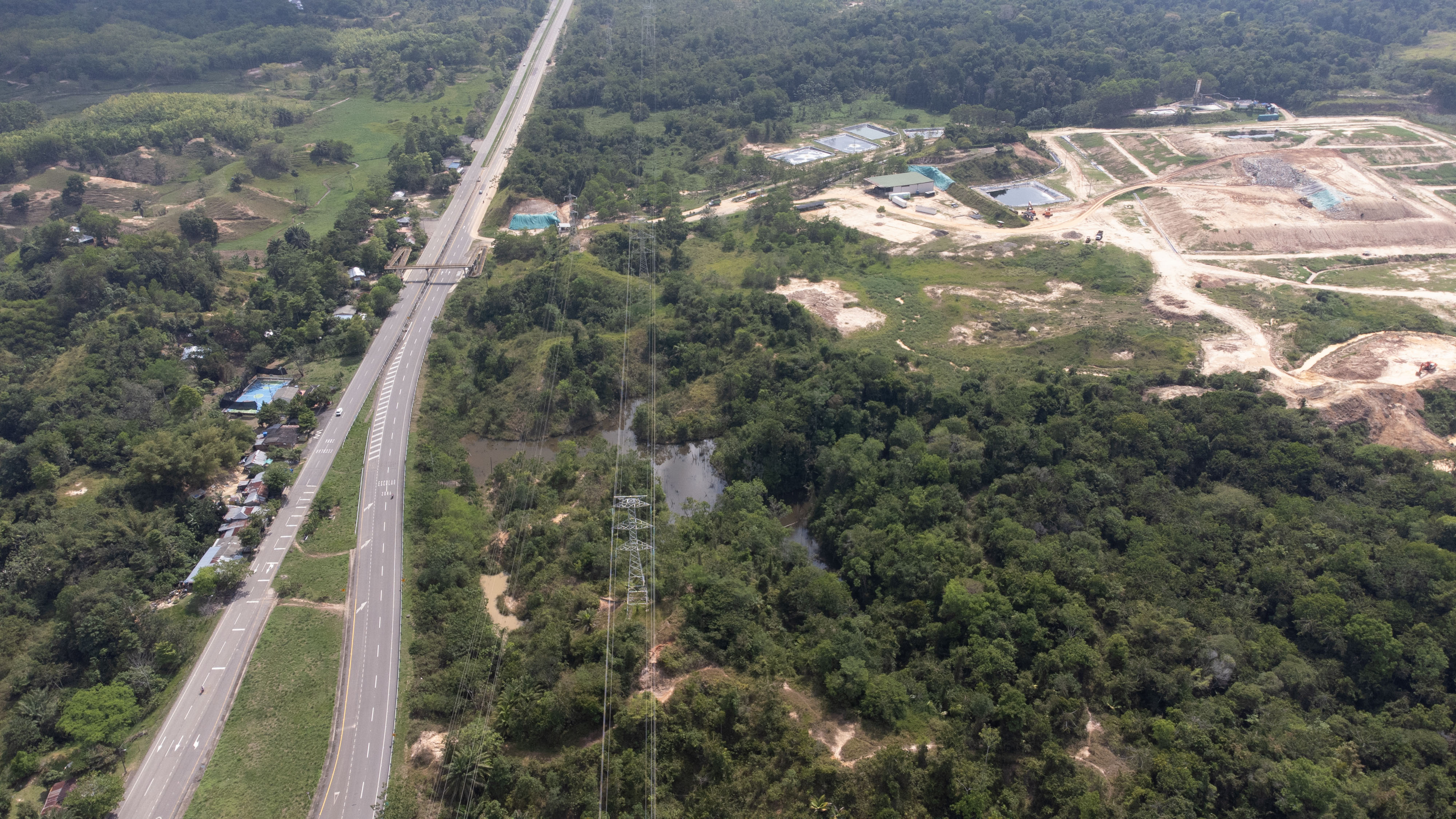 Small structures can be seen in a green forest, punctuated by a large roadway and a landfill