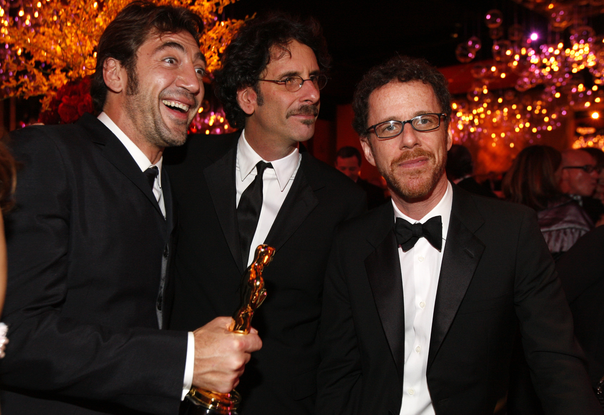 Three men in tuxedos and suits pose for a photo against a darkened background.