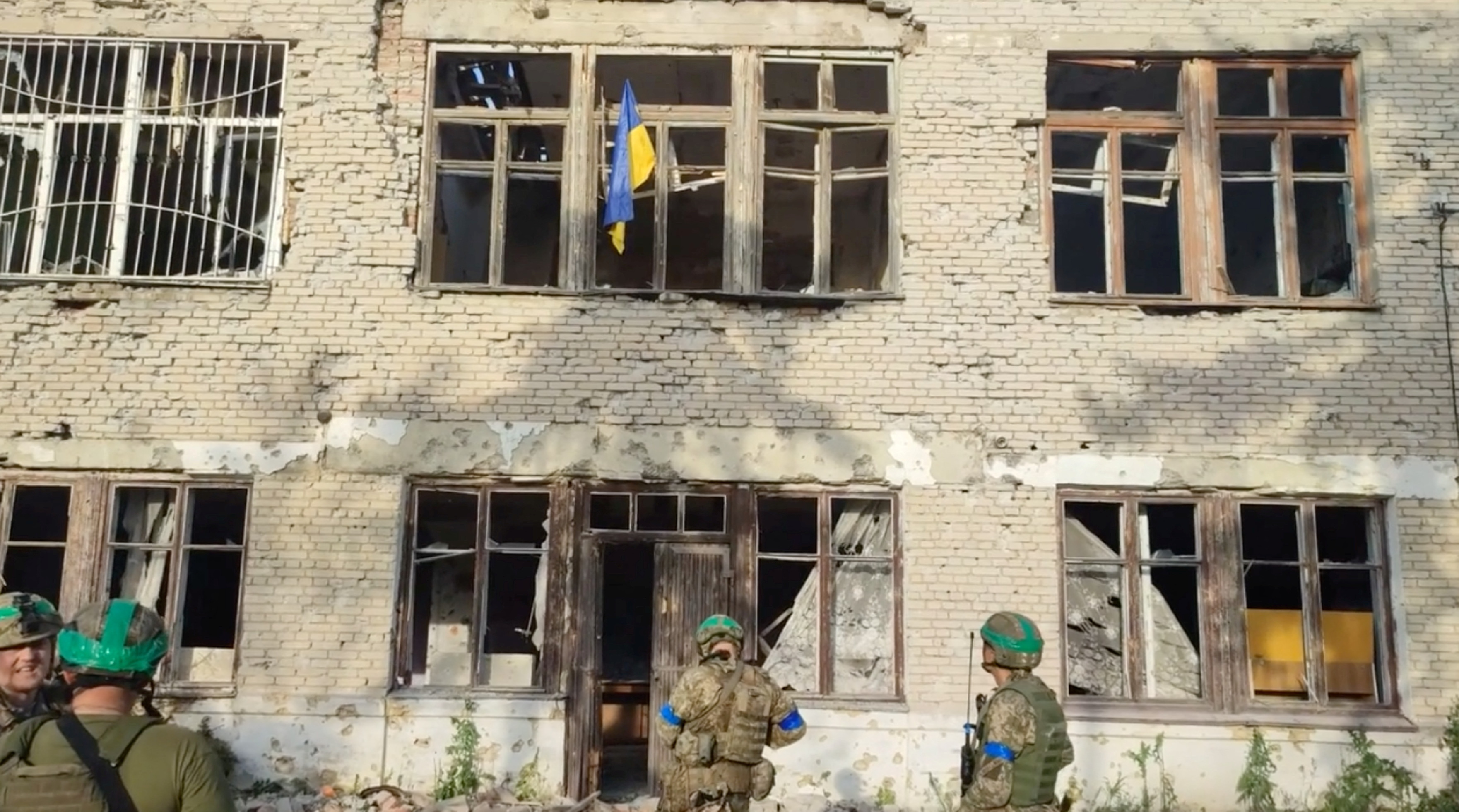 Ukrainian soldiers stand in front of a building with a Ukrainian flag on it, during an operation that claims to liberate the first village amid a counter-offensive, in a location given as Blahodatne