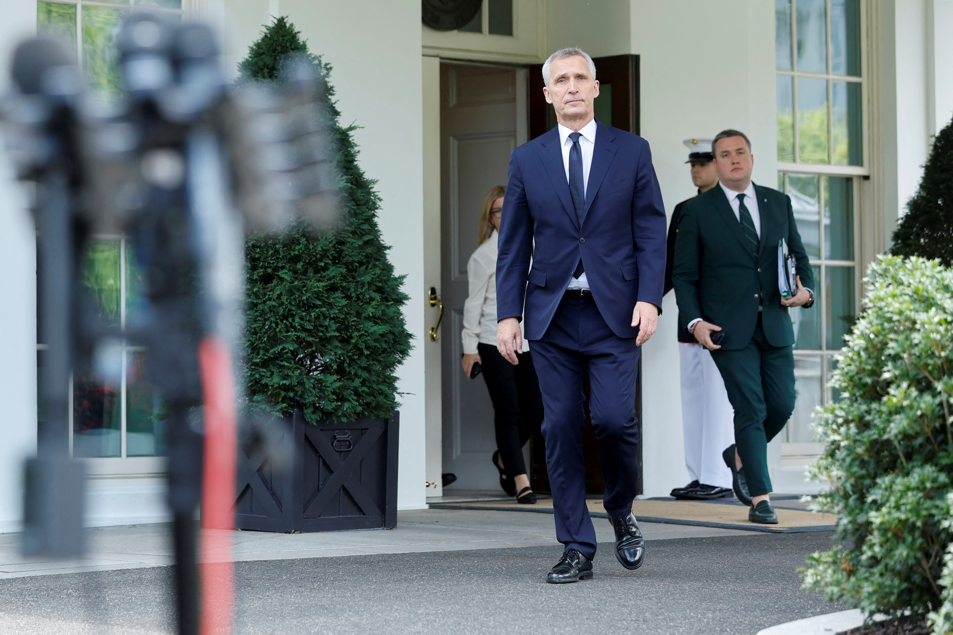 A man in a navy blue suit walks out of a government building.