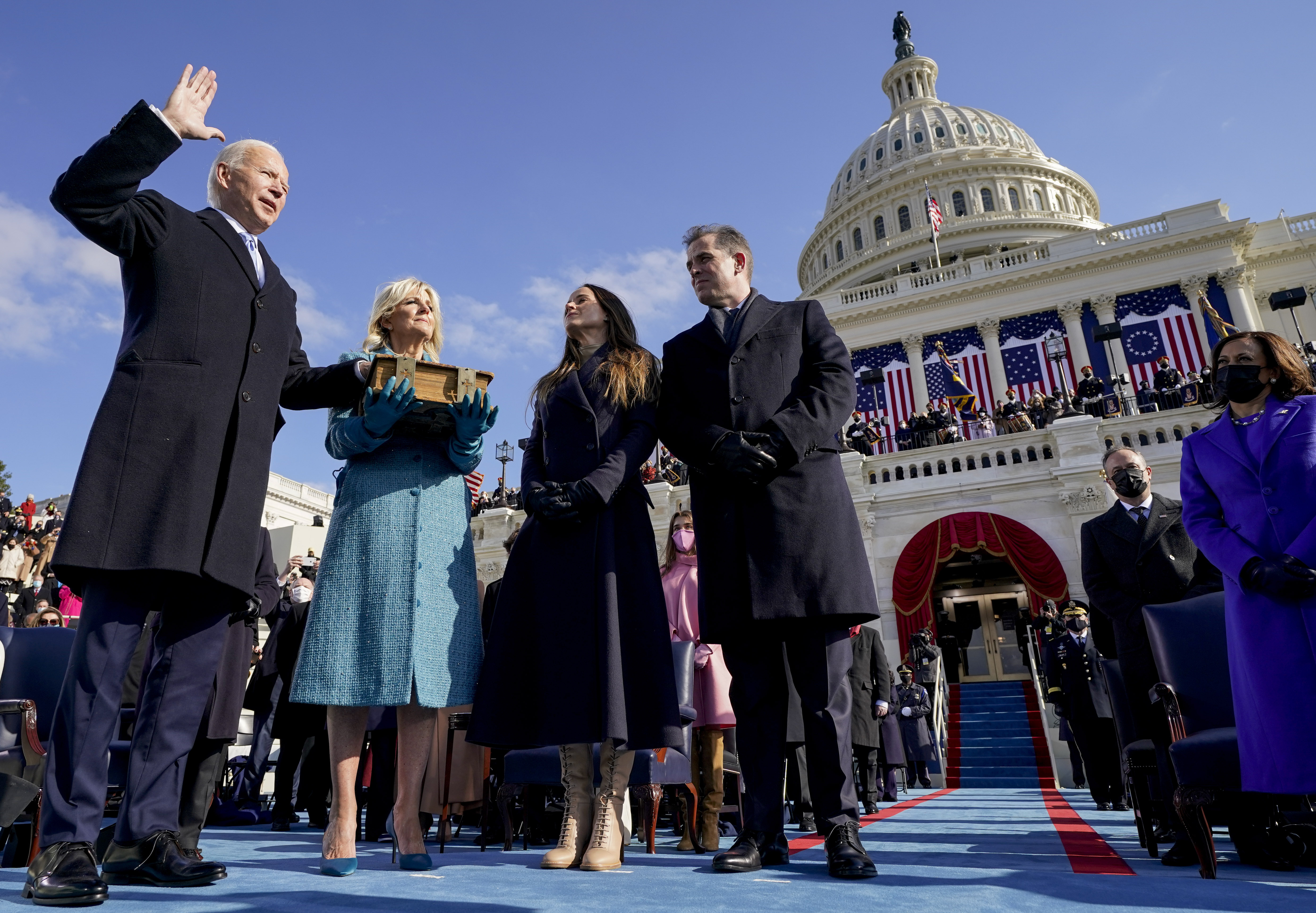 A man raises his right hand and places another on a book on the steps of the Capitol to be sworn in as president. His family looks on.
