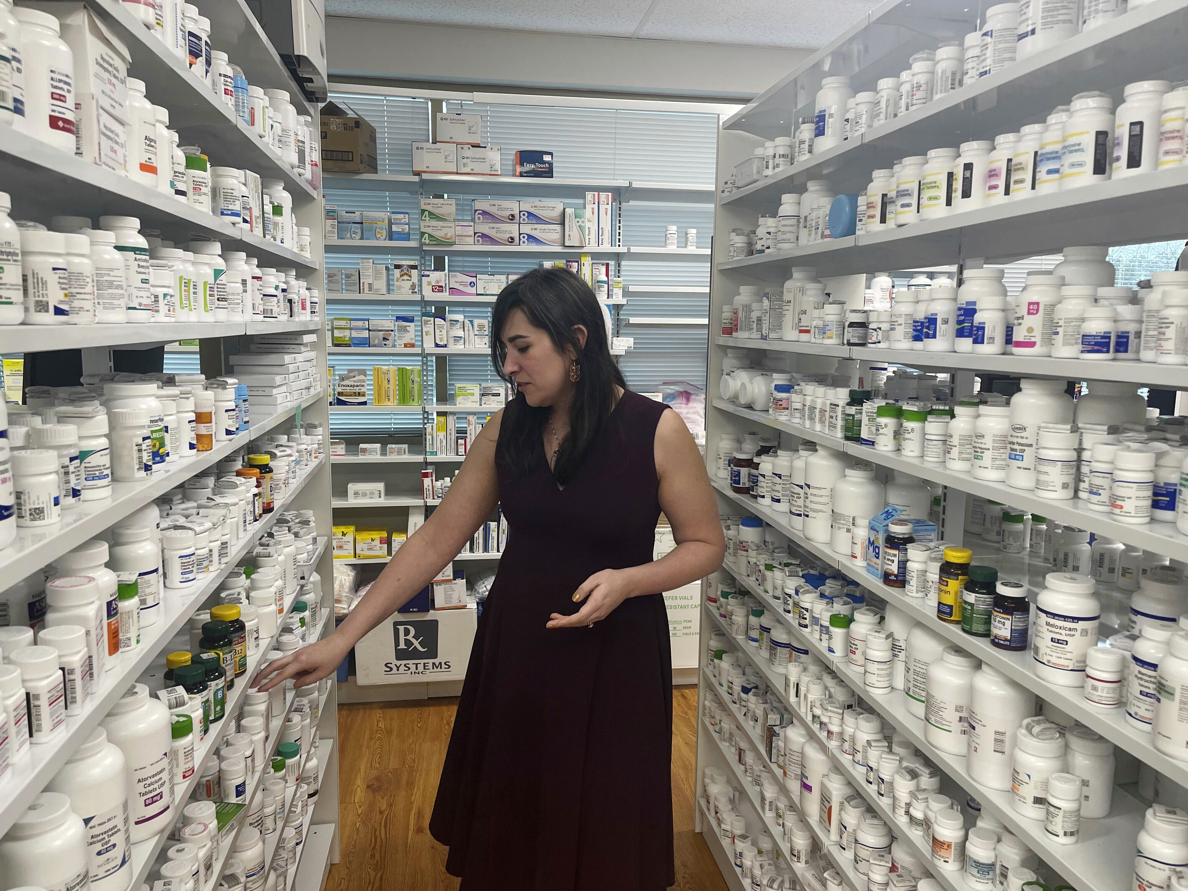 A woman walks through the aisles of a pharmacy, with shelves full of medication.