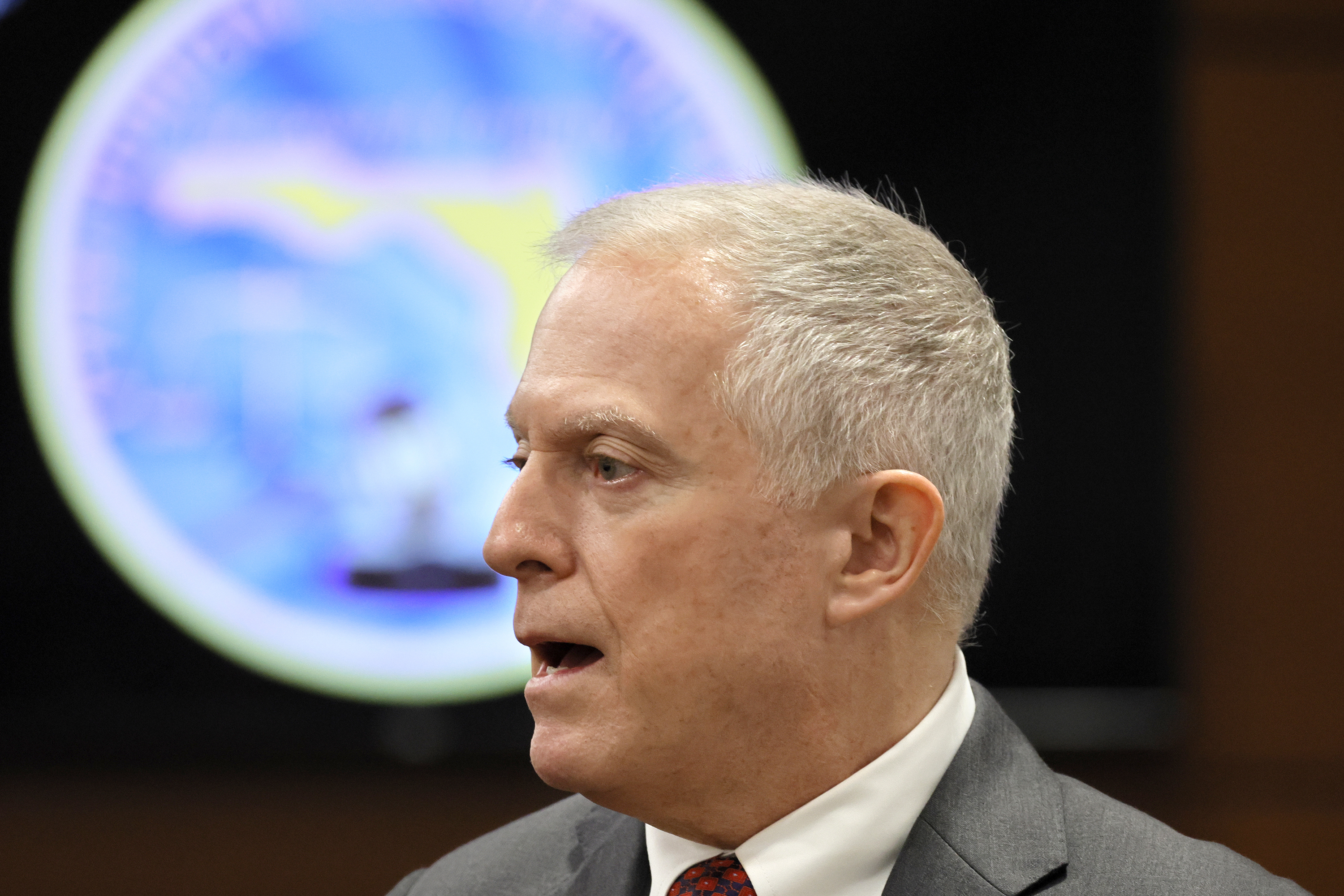 A close-up of Steven Klinger, dressed in a grey suit, with a Florida seal behind him.