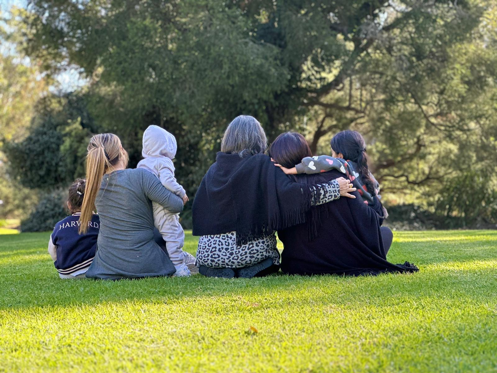 A family of Iranian refugees sitting outside together in a park. One young woman is holding her toddler