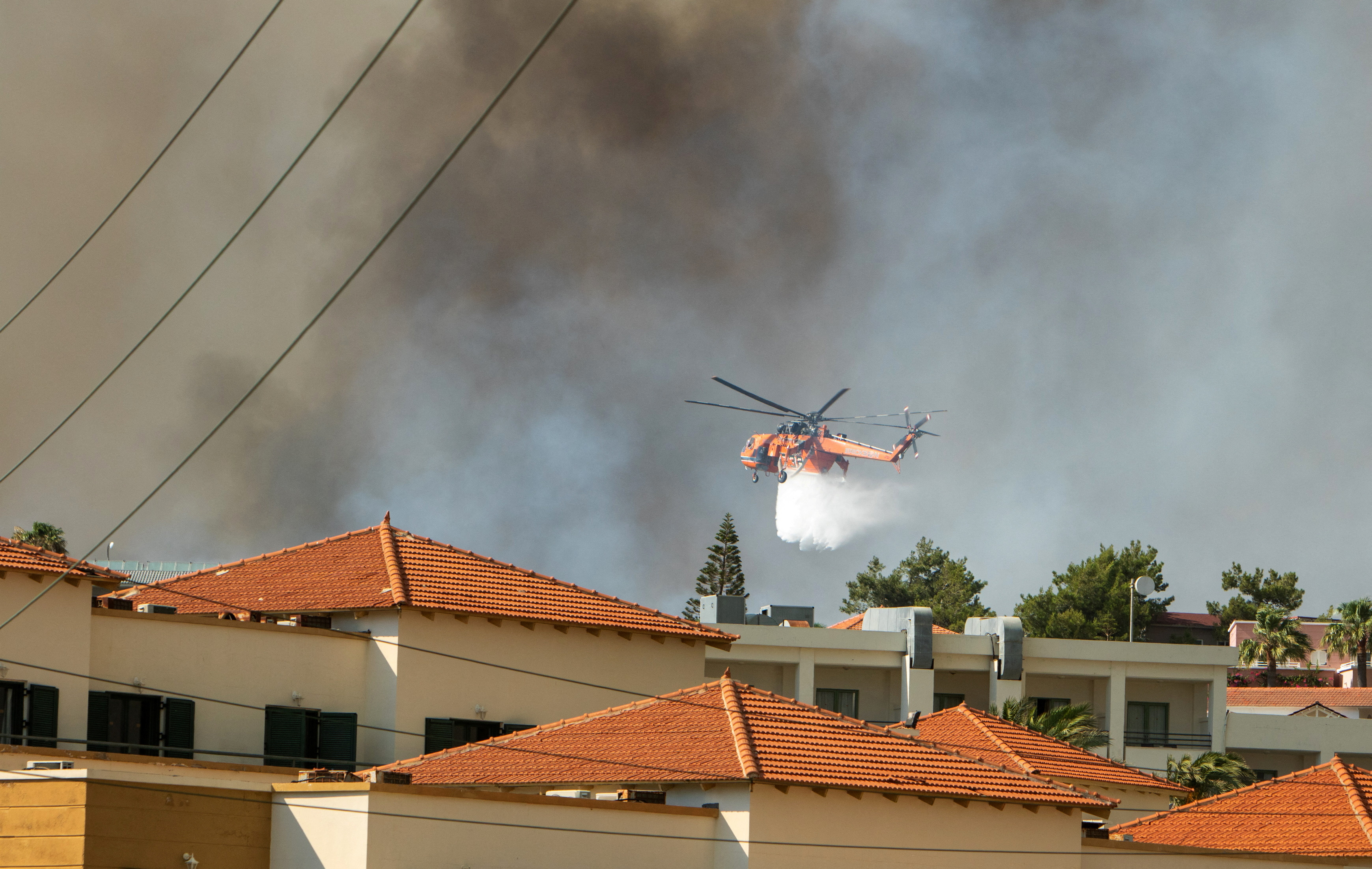 A firefighting helicopter drops water over a wildfire burning near Lindos