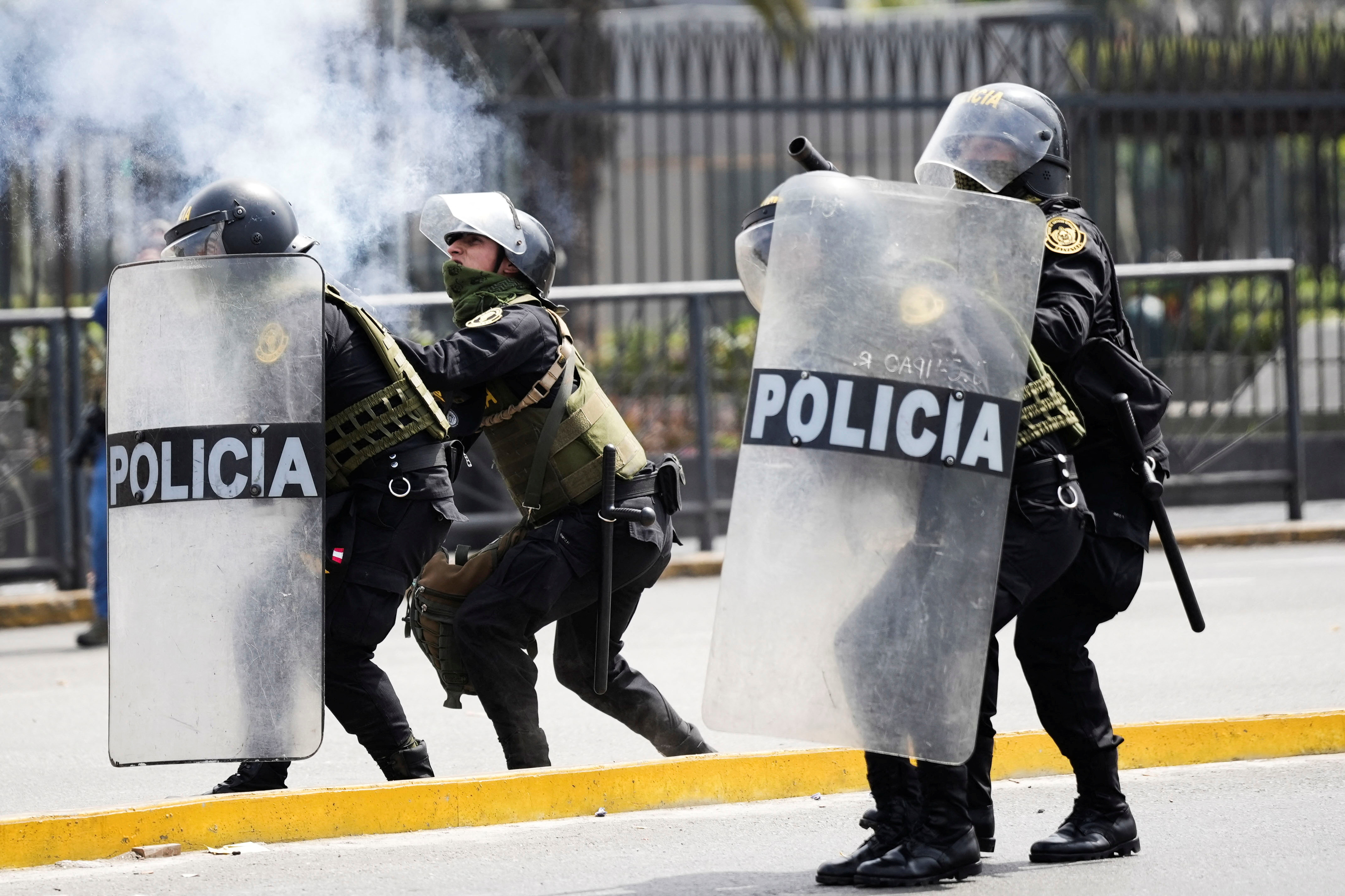 Riot police, dressed in helmets and all black, hold plastic shields and launch tear gas.