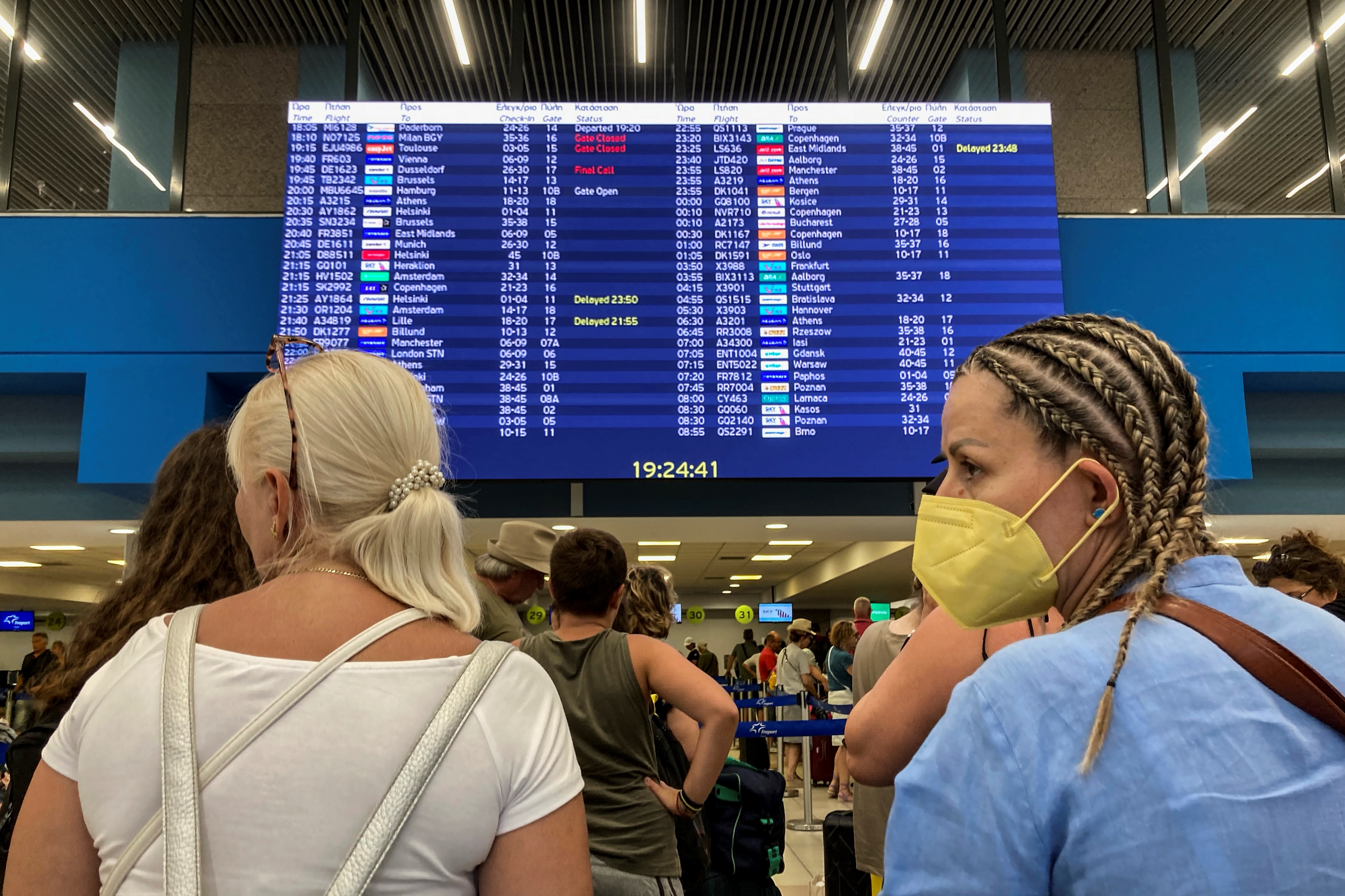 Tourists stand in front of an information board at the airport's departure hall as evacuations are underway due to wildfires, on the Greek island of Rhodes