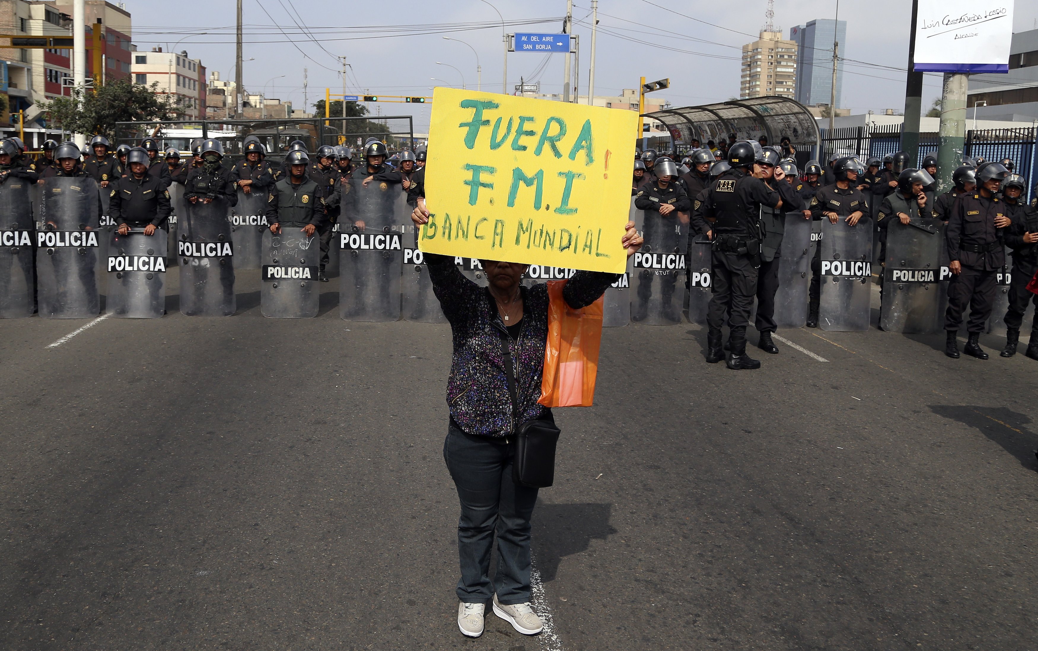 A protestor holds a sign that reads in Spanish "Get out IMF, World Bank" near police blocking protesters from getting any closer to the venue where the IMF and World Bank are holding their annual meetings in Lima, Peru, Friday, Oct. 9, 2015. More than 60 percent of Peruvians workers are in the informal economy, according to U.N. figures, spending on health care and education are below regional averages and most government revenues come not from income tax but rather taxes on sales and consumption, putting the burden disproportionately on the poor in the region with the world's most unequal wealth distribution. (AP Photo/Geraldo Caso Bizama)