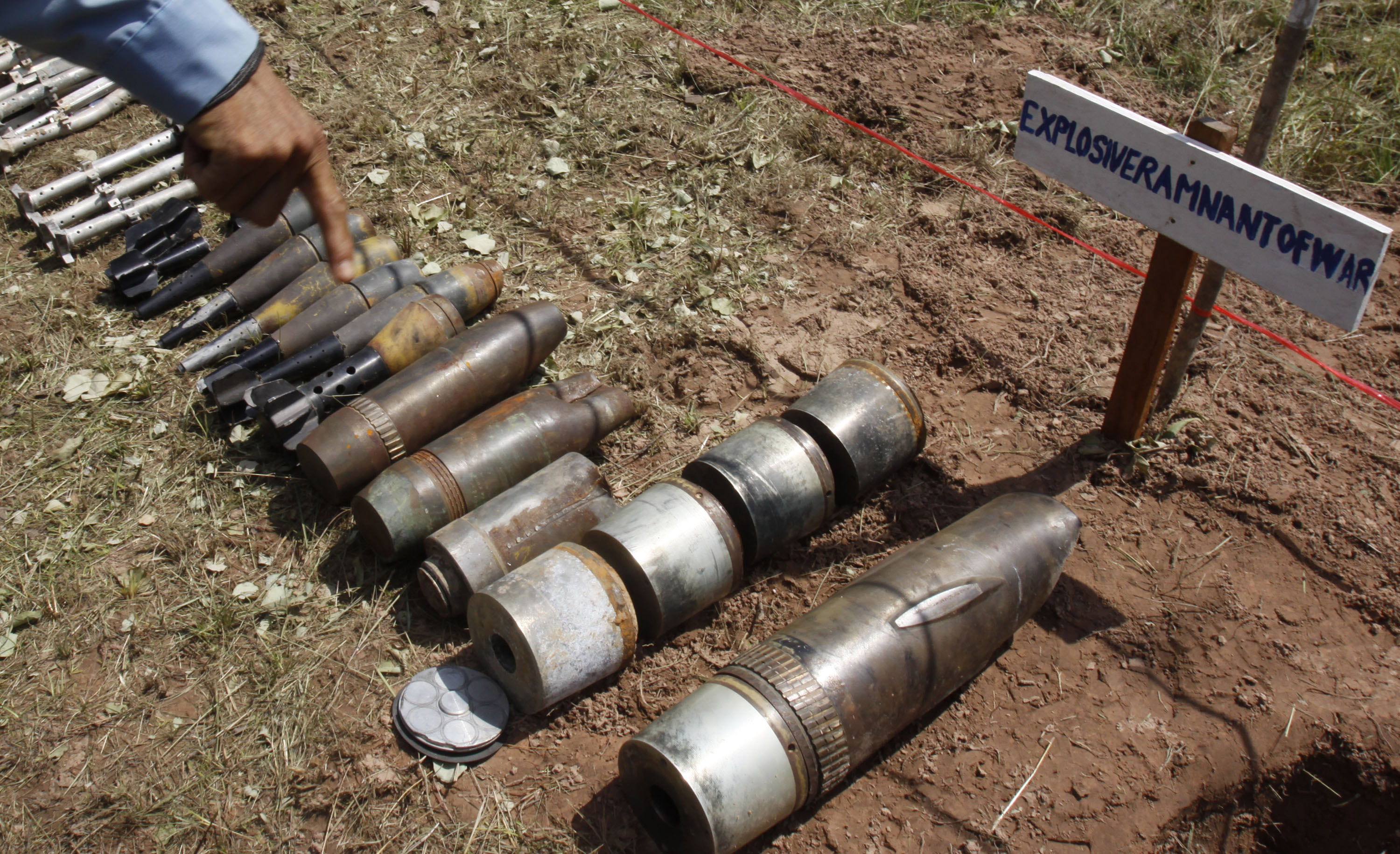 FILE - A Cambodian demining expert points to unexploded bombs displayed on the ground before a destruction ceremony in Preah Vihear province, about 245 kilometers (152 miles) north of Phnom Penh, Cambodia, Thursday, July 7, 2011. Three demining experts from the Cambodian Self Help Demining (CSHD), a non-government demining organization based in Cambodia, were killed Monday, Jan. 10, 2022, while trying to defuse a anti-tank mine in the Chum Chan District, Preah Vihear Province. (AP Photo/Heng Sinith, File)