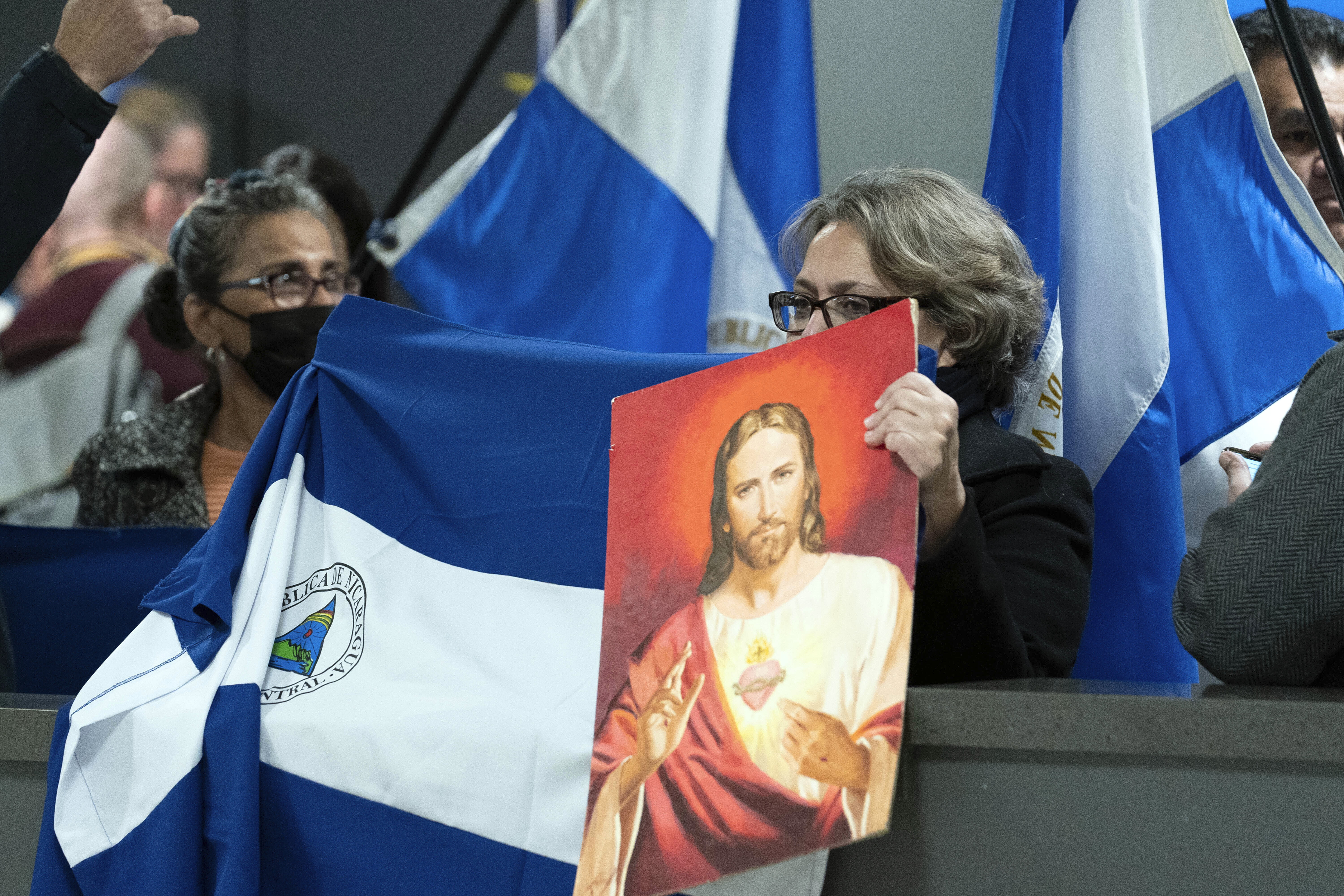 A woman holds up a portrait of Jesus, while another drapes a Nicaraguan flag across the barrier at the arrival gate at an airport in Washington, DC.