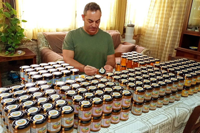 A photo of someone labelling a jar of honey with a table full of jars of honey in front of them.