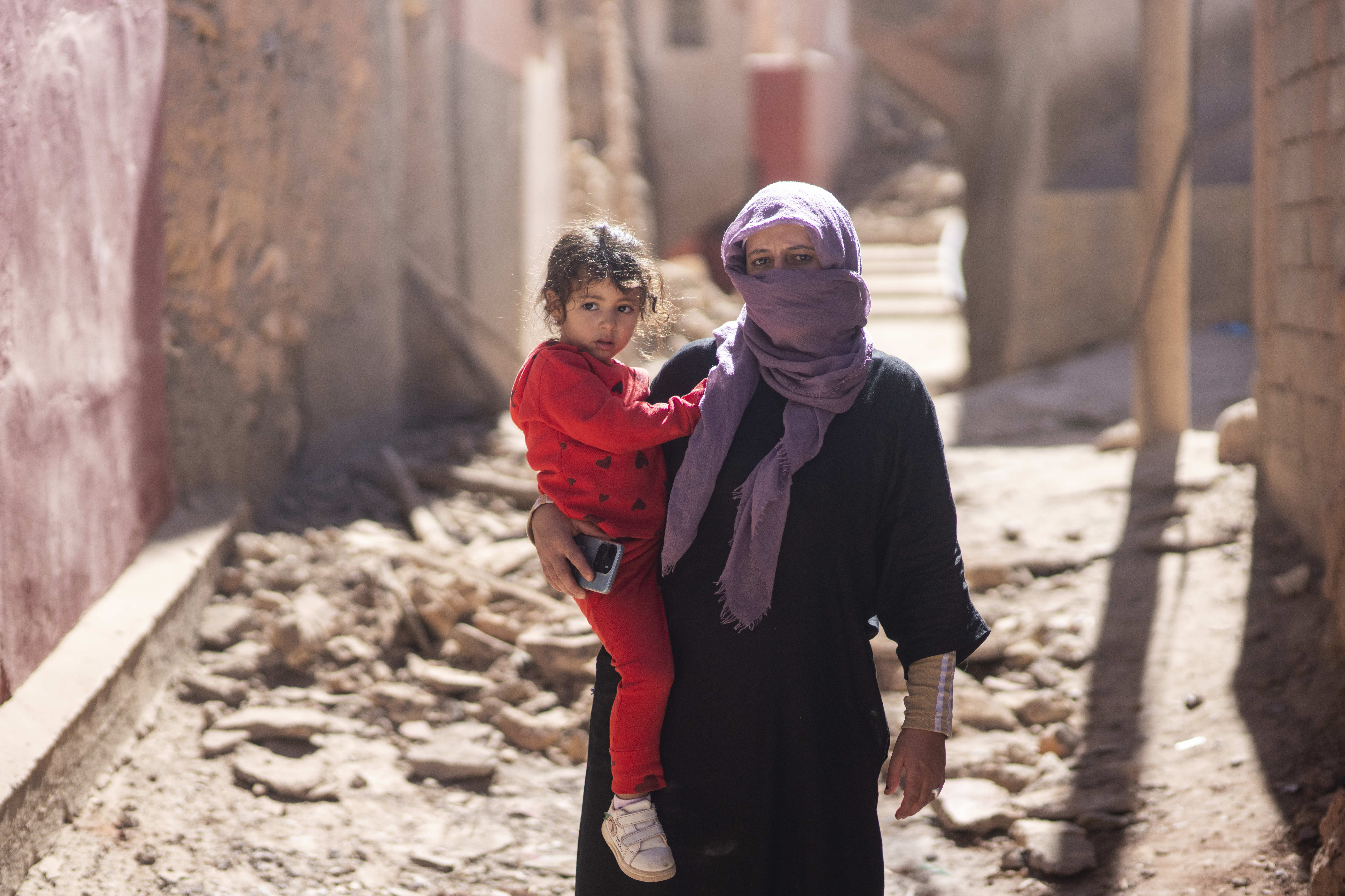 mother and daughter stand in the middle of rubble from earthquake