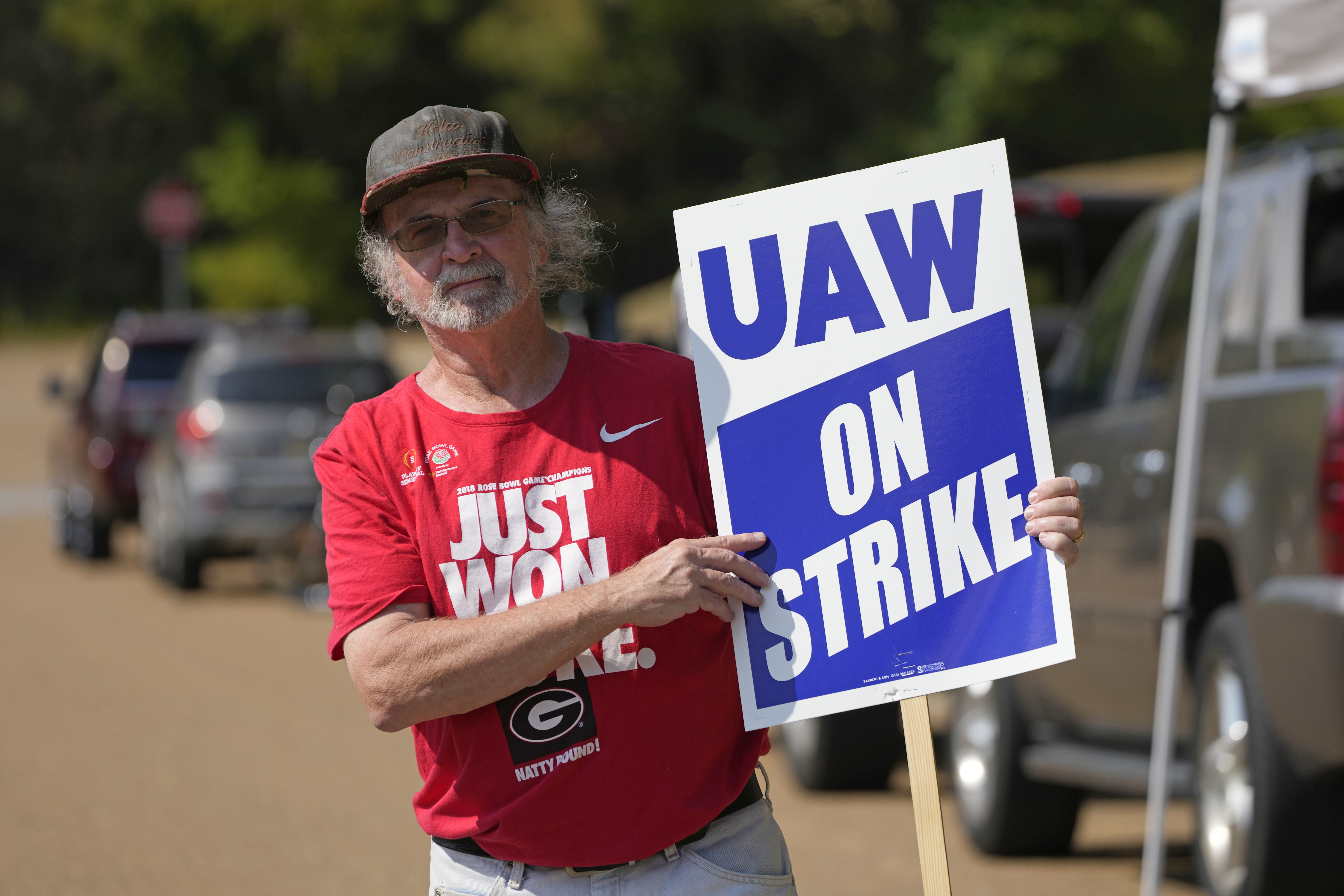 United Auto Workers member Ron Oglesby holds a picket sign outside the General Motors Customer Care and After-Sales facility in Brandon, Miss., Friday, Sept. 22, 2023. Unionized workers joined others in new nationwide walkouts as the labor standoff continues. Oglesby wears a hat and a red shirt, and he points to his picket sign that reads, "UAW on strike."