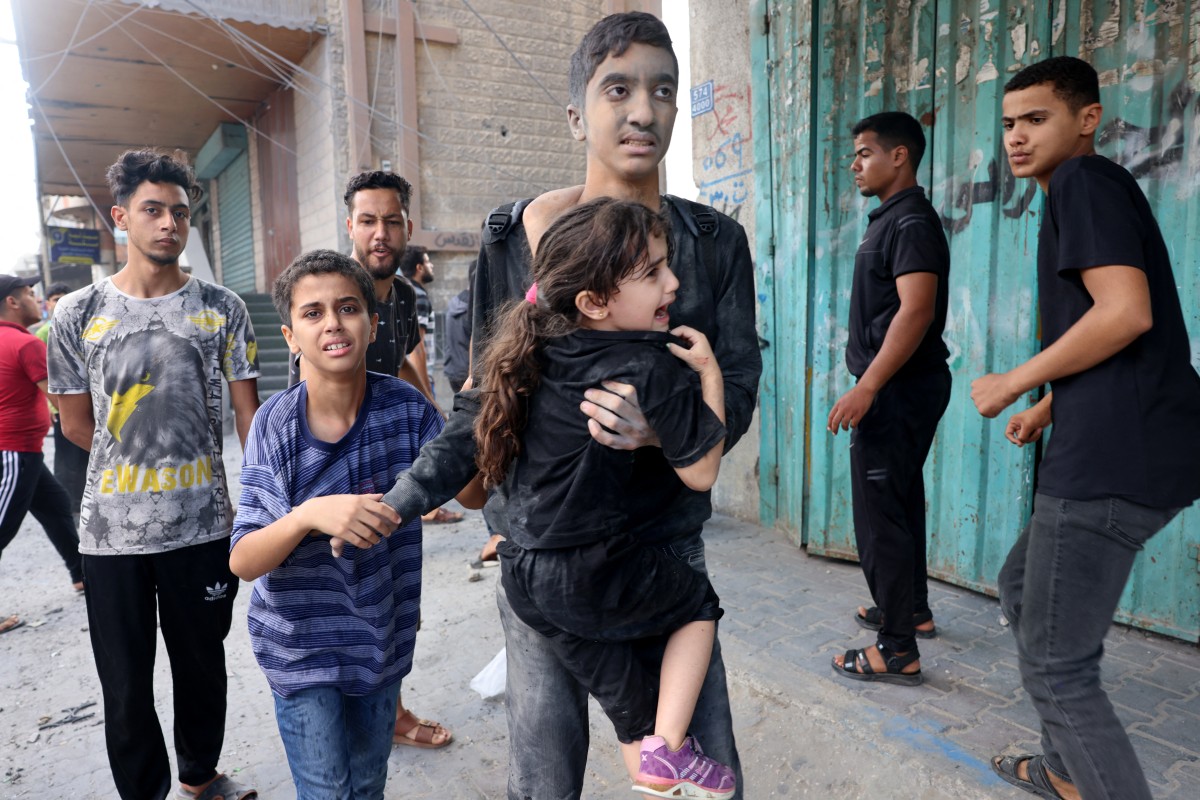 A young man carries a little girl following an Israeli strike, as battles between Israel and the Hamas movement continue for the sixth consecutive day in Rafah