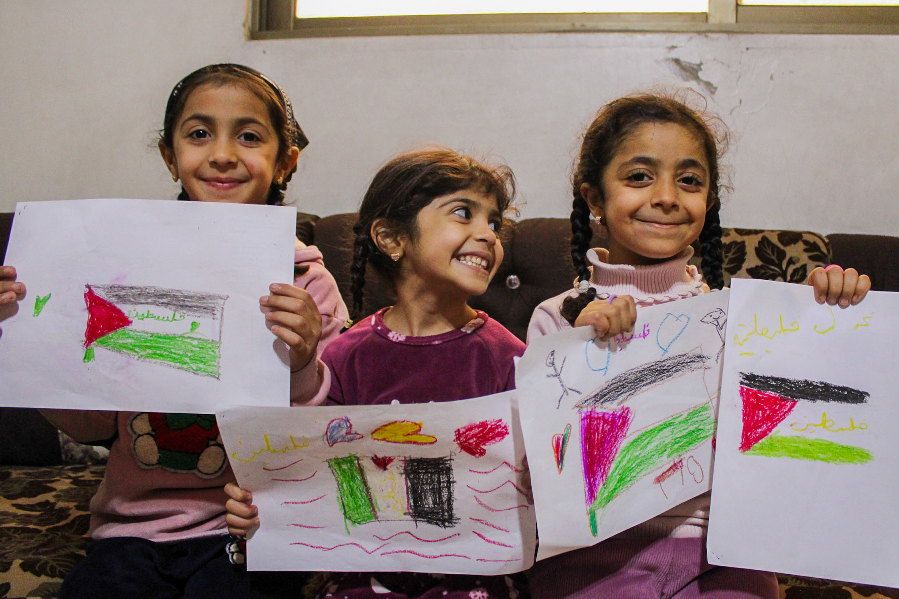 Alaa’s daughters hold up their drawings of the Palestinian flag