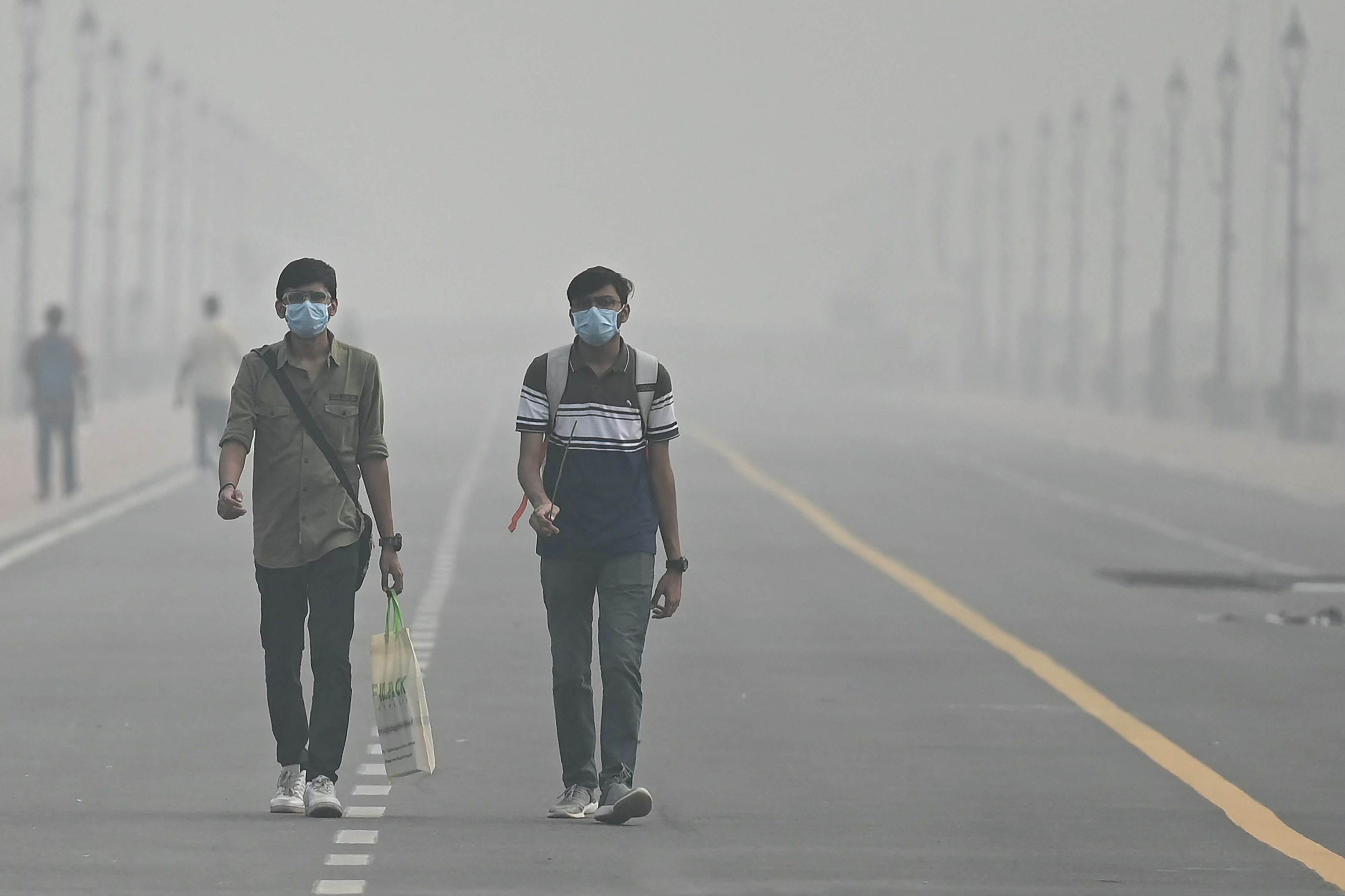 People wearing face masks walk along the Kartavya Path amid heavy smoggy conditions in New Delhi on November 5