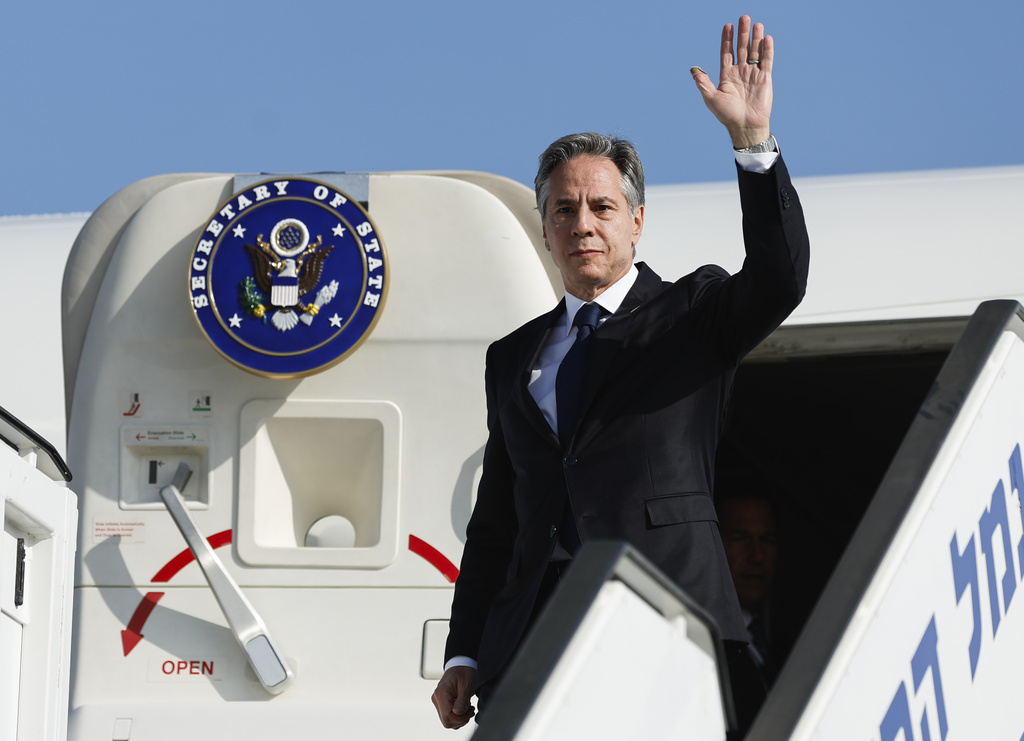 Antony Blinken waves as he steps off a plane