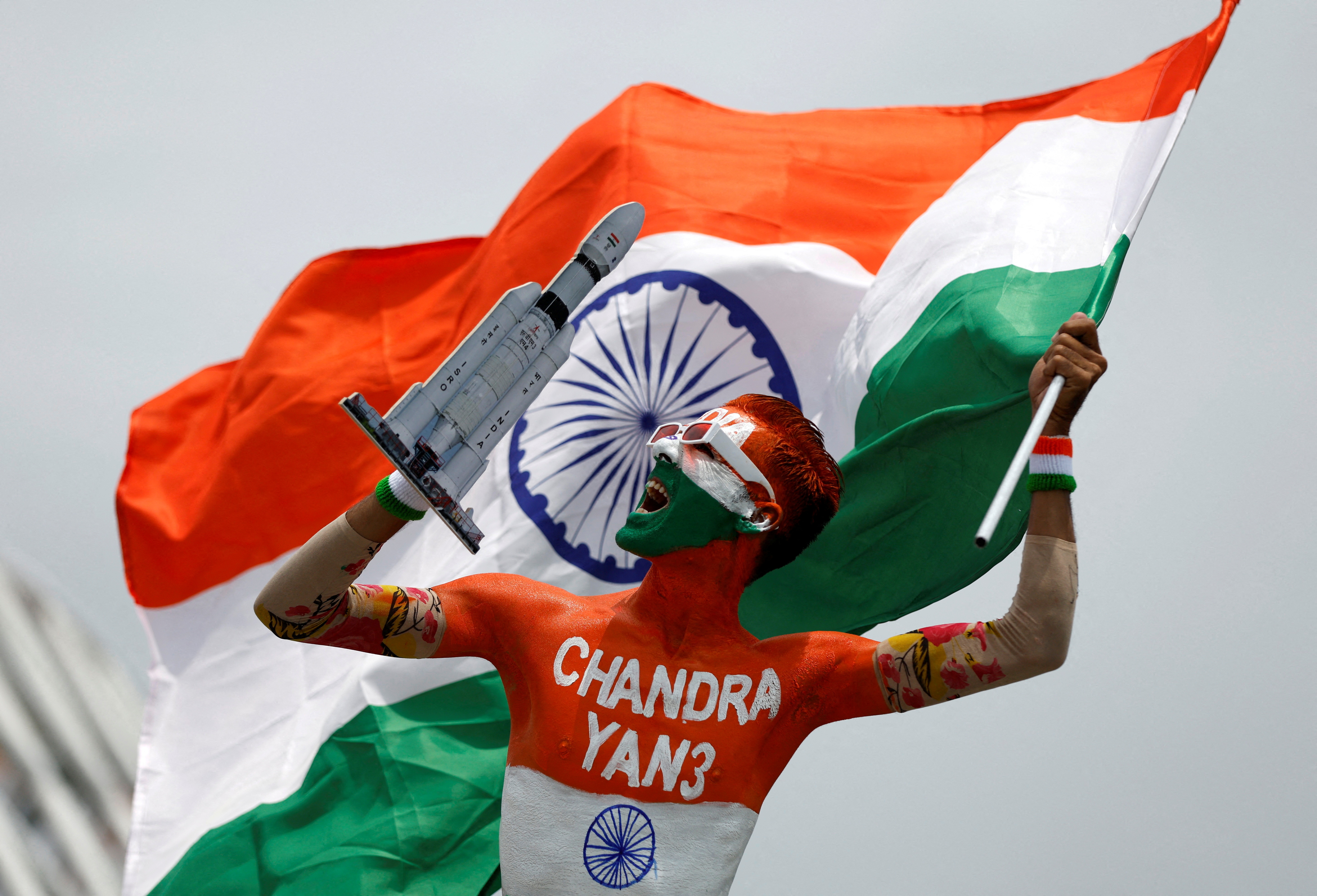Arun Haryani, an enthusiast with his body painted in tri-colours reacts as he holds up a model of LVM3 M4 which was used in launching of Chandrayaan-3 spacecraft on the eve of its moon landing, in Ahmedabad, India, August 22