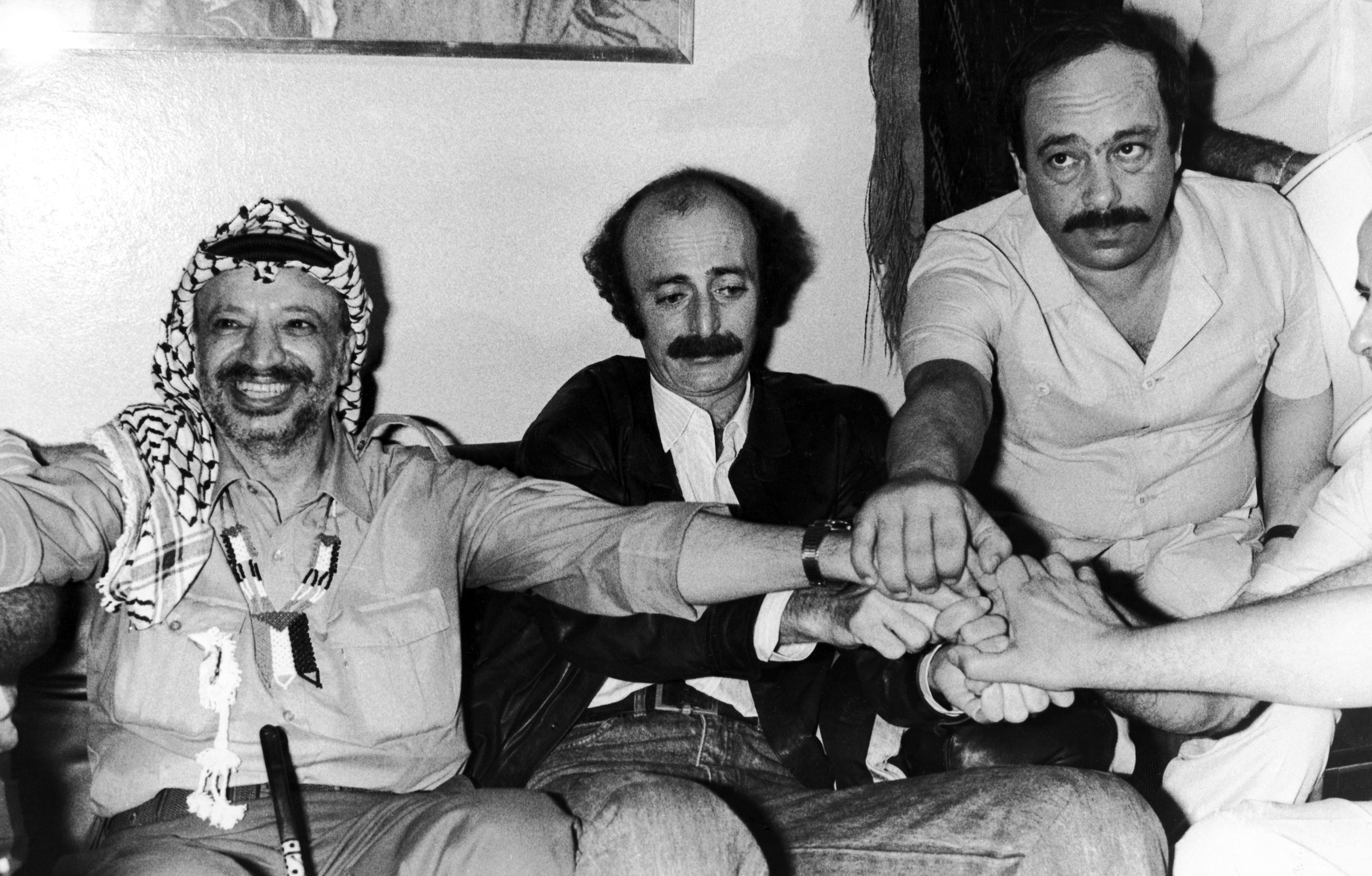 PLO chairman Yasser Arafat, left, with Lebanese leftist leader Walid Jumblatt, center, and an unidentified man, get their hands together in a gesture to show reporters, at a press conference, in Beirut, on Aug. 30, 1982, that they will stick together. Arafat made his farewell visit to Jumblatt before he leaves the Lebanese capital by ship to an unknown destination. (AP Photo/Langevin)