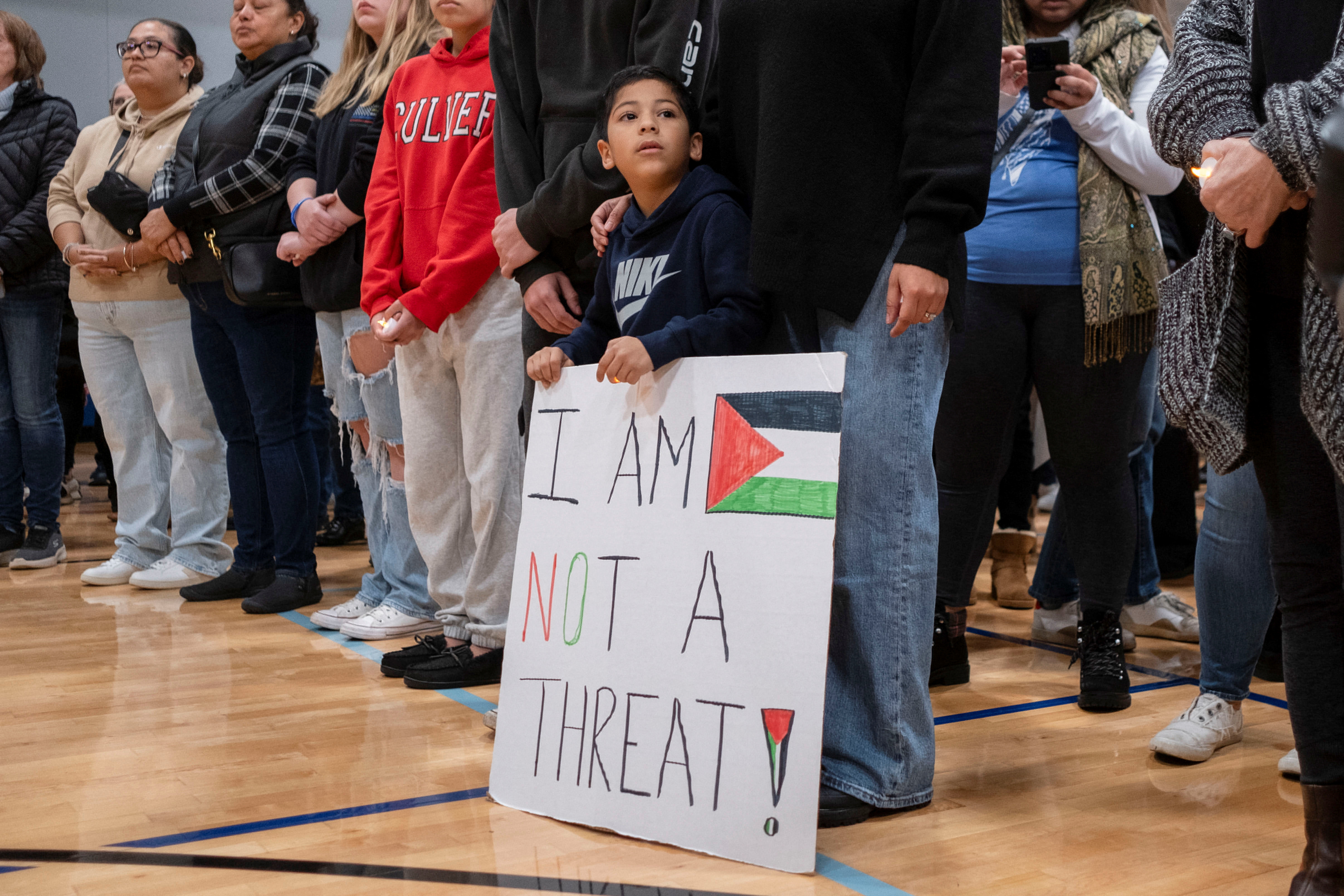 A boy holds a sign reading, 'I am not a threat!' at a vigil to mourn the killing of a Palestinian-American boy near Chicago