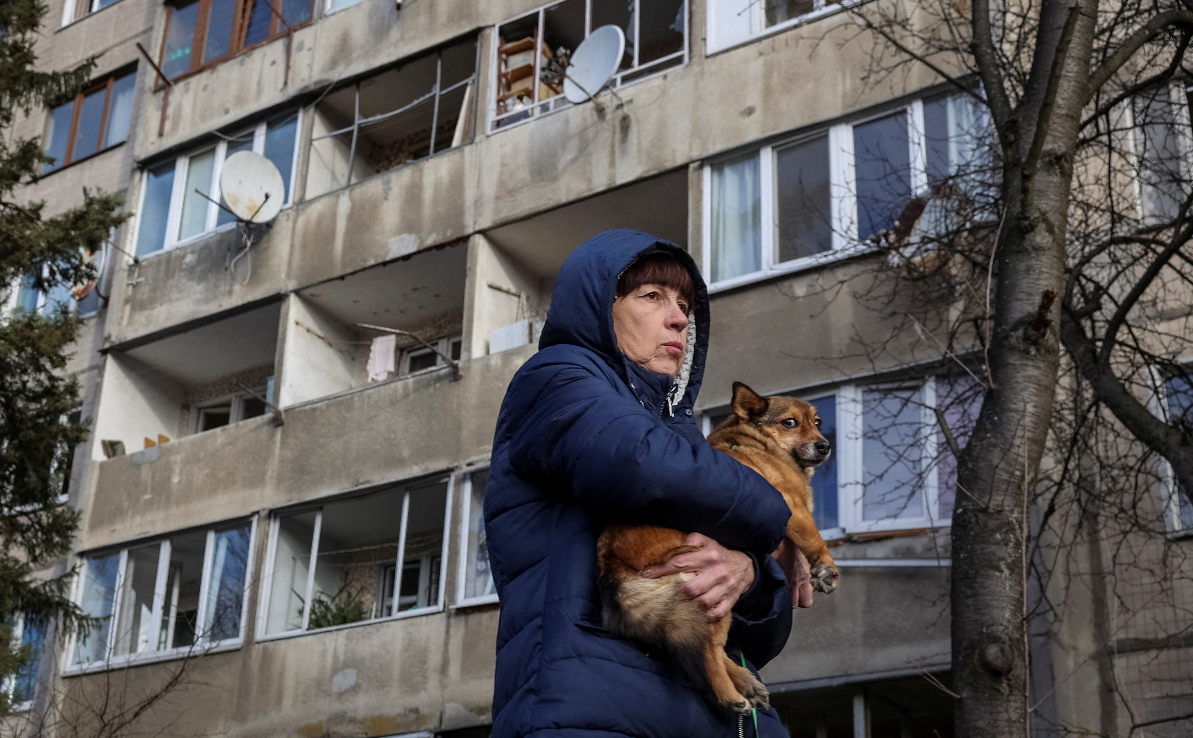 A local resident holds her dog as she stands near her apartment building damaged