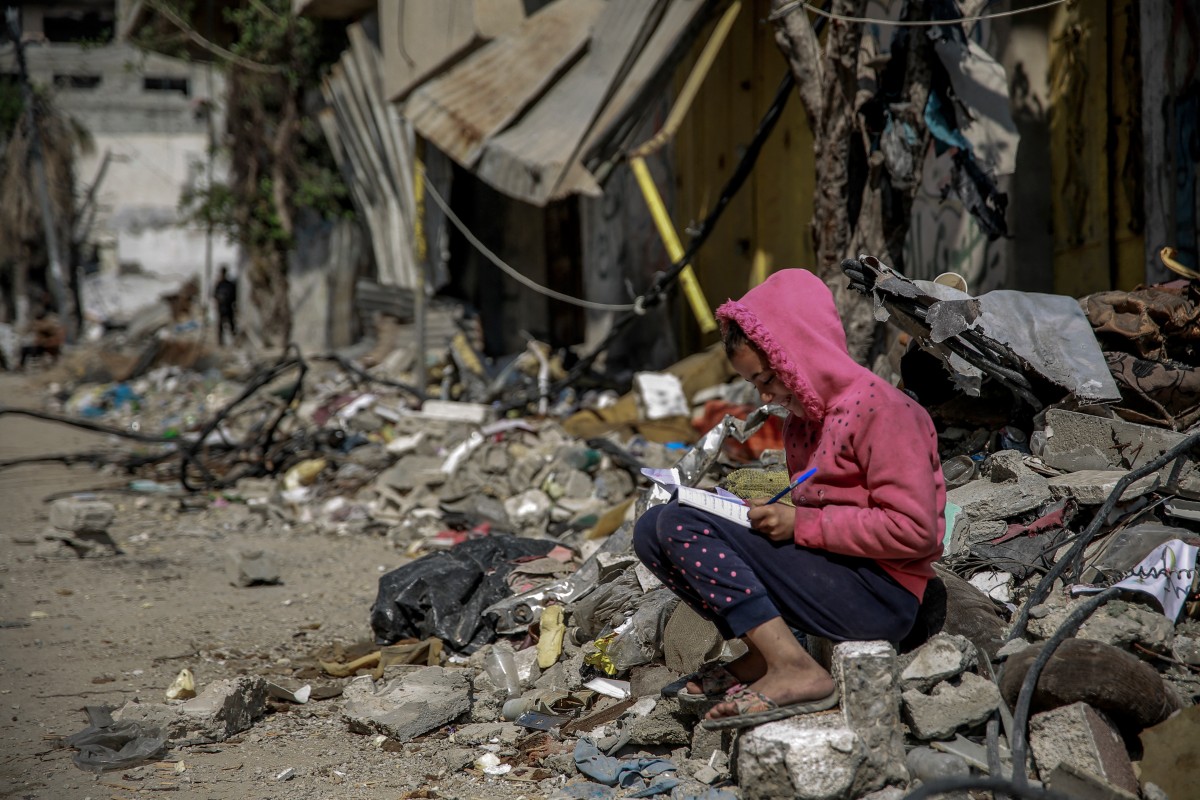 A Palestinian child reacts as she sits amid debris of buildings