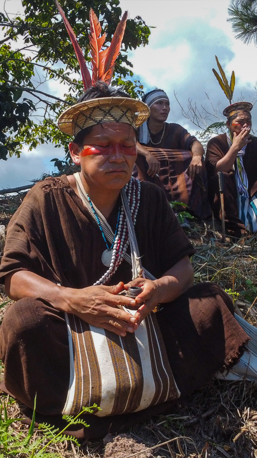 Ashaninka leader Tsitsiri Samaniego sits crosslegged on a hillside, with his family in the background.