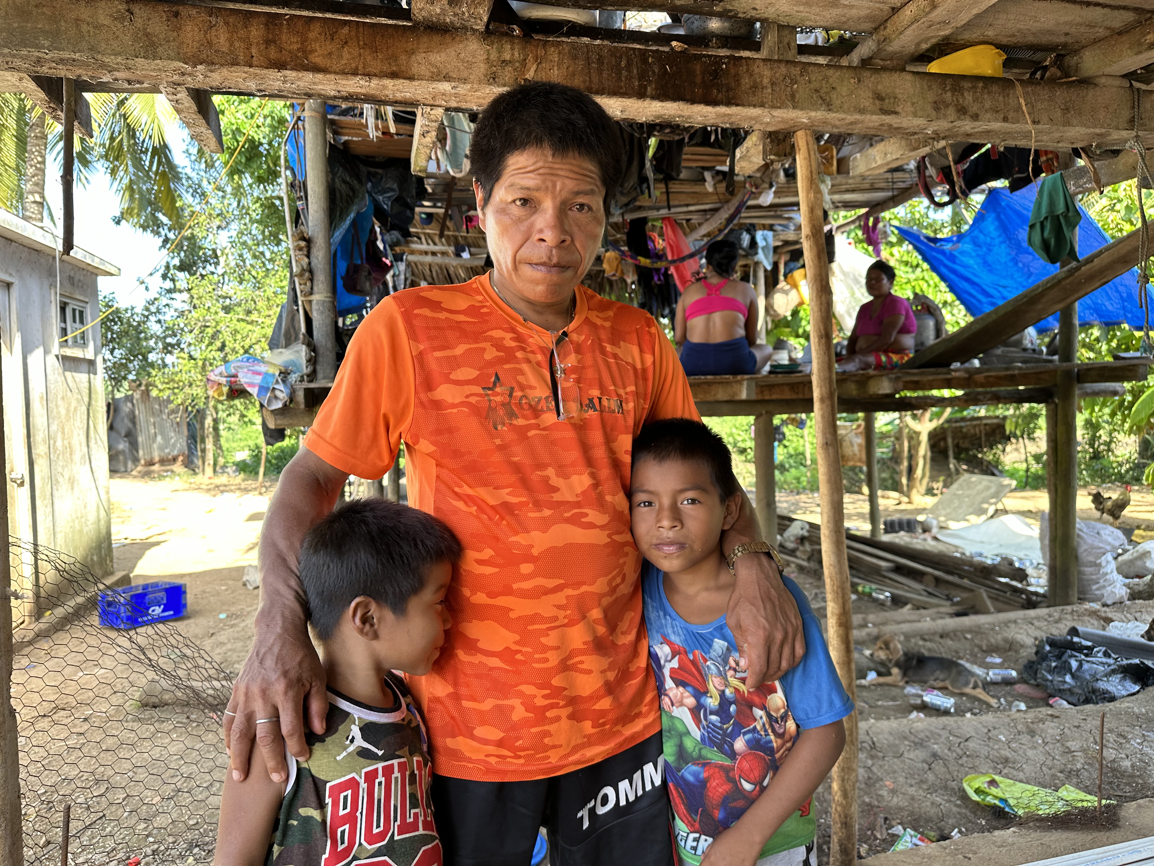 A man in an orange T-shirt poses for a photo, with his two children by his side.
