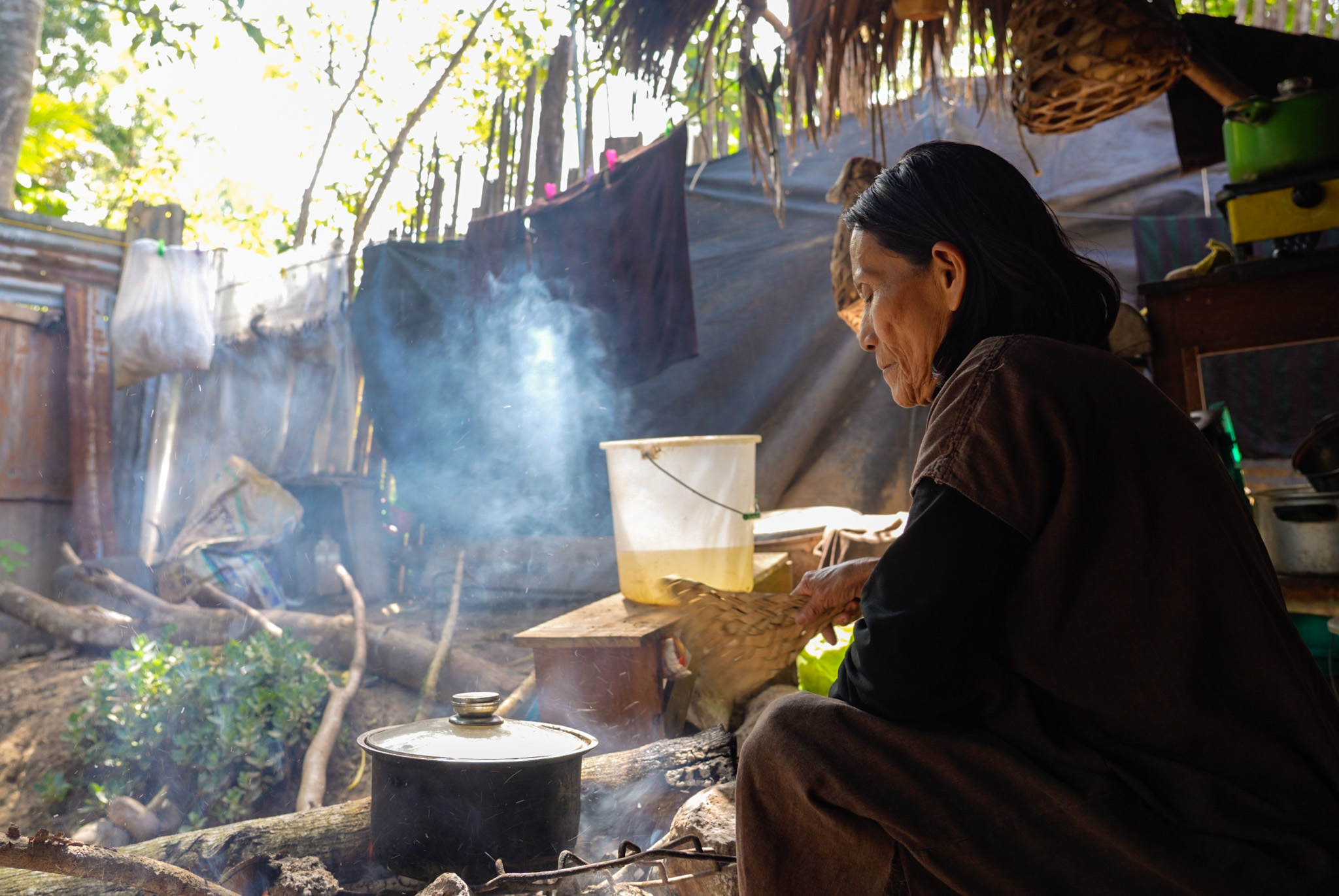 Pachaka, an Indigenous elder, sits in front of a pot boiling on an open fire.
