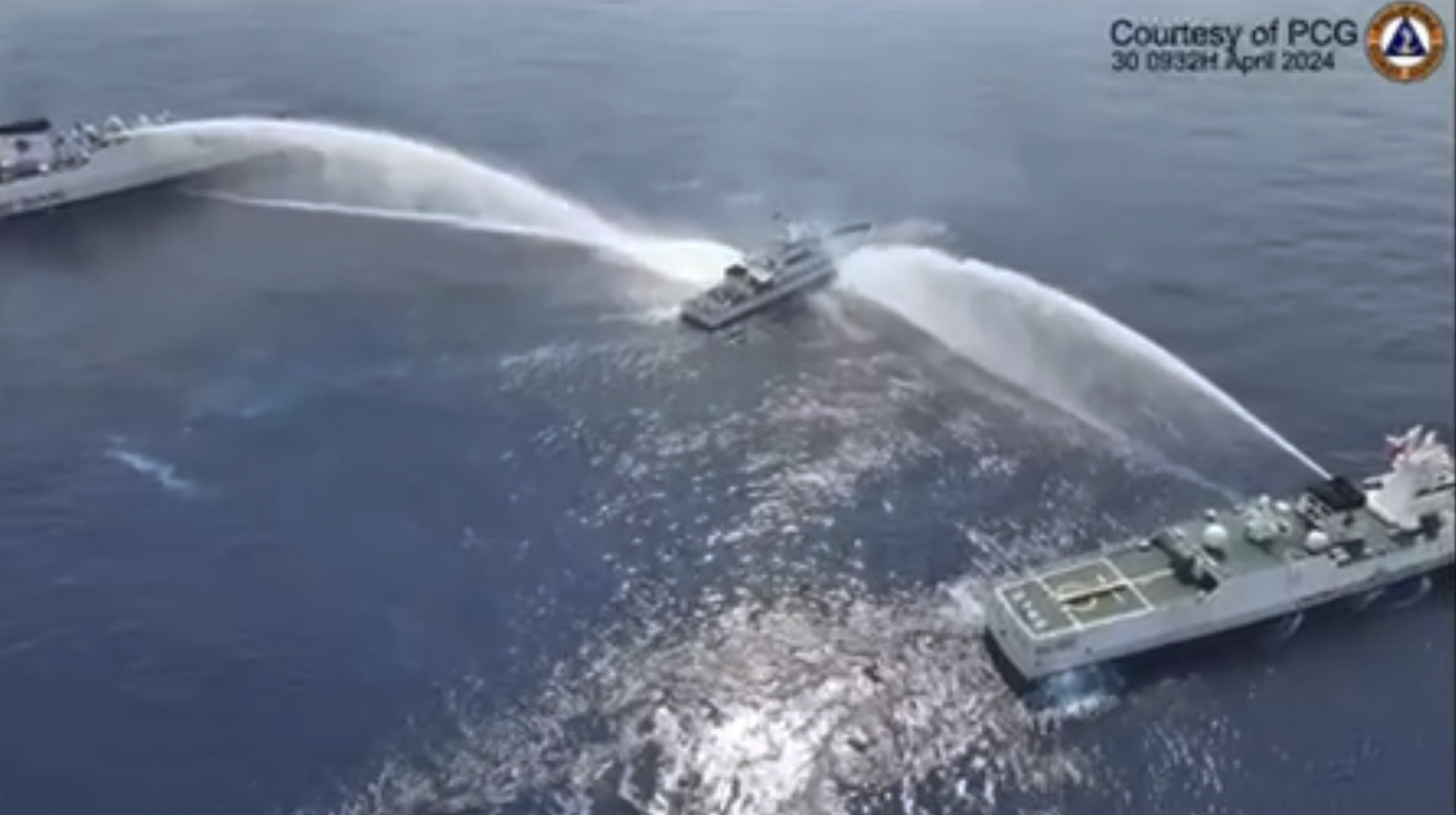 A screen grab showing two Chinese coast guard ships firing water cannon at a Filipino ship. The Filipino ship is between the two Chinese ships