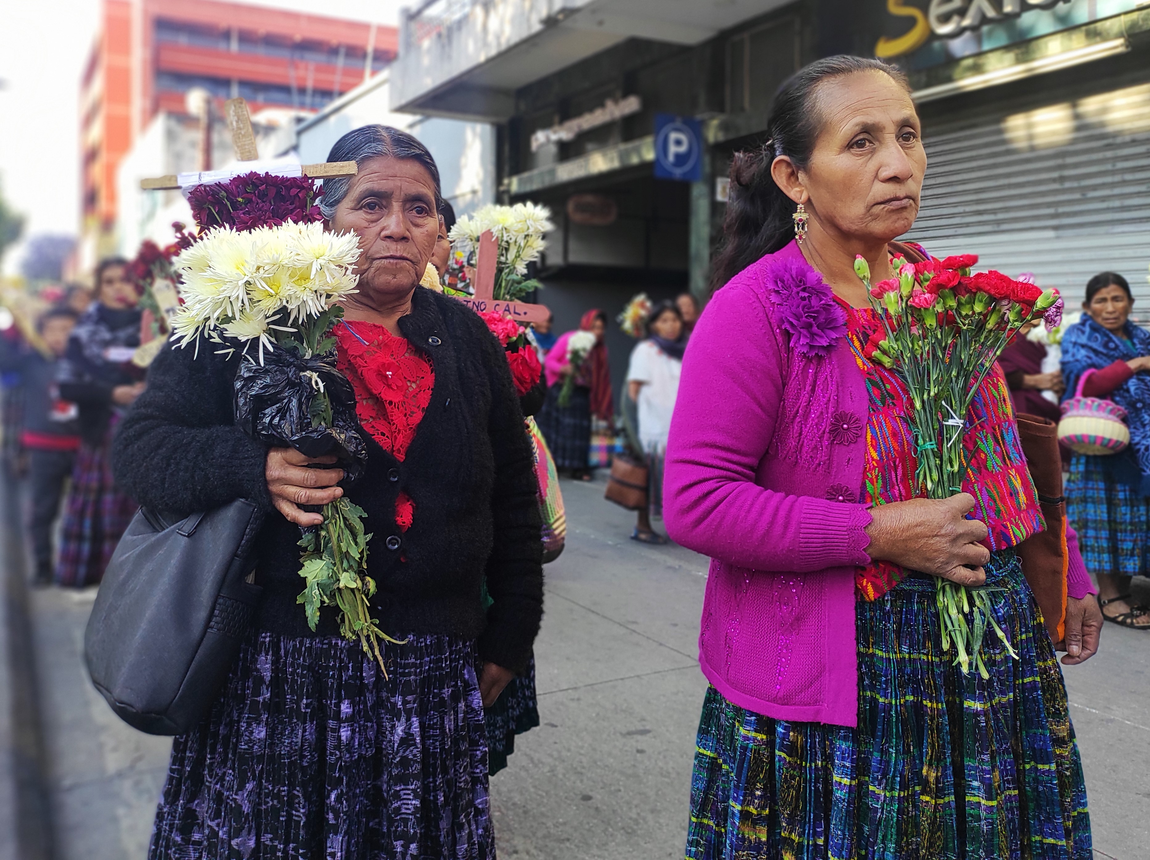 Indigenous women in Guatemala hold bouquets of flowers as they walk through the streets.