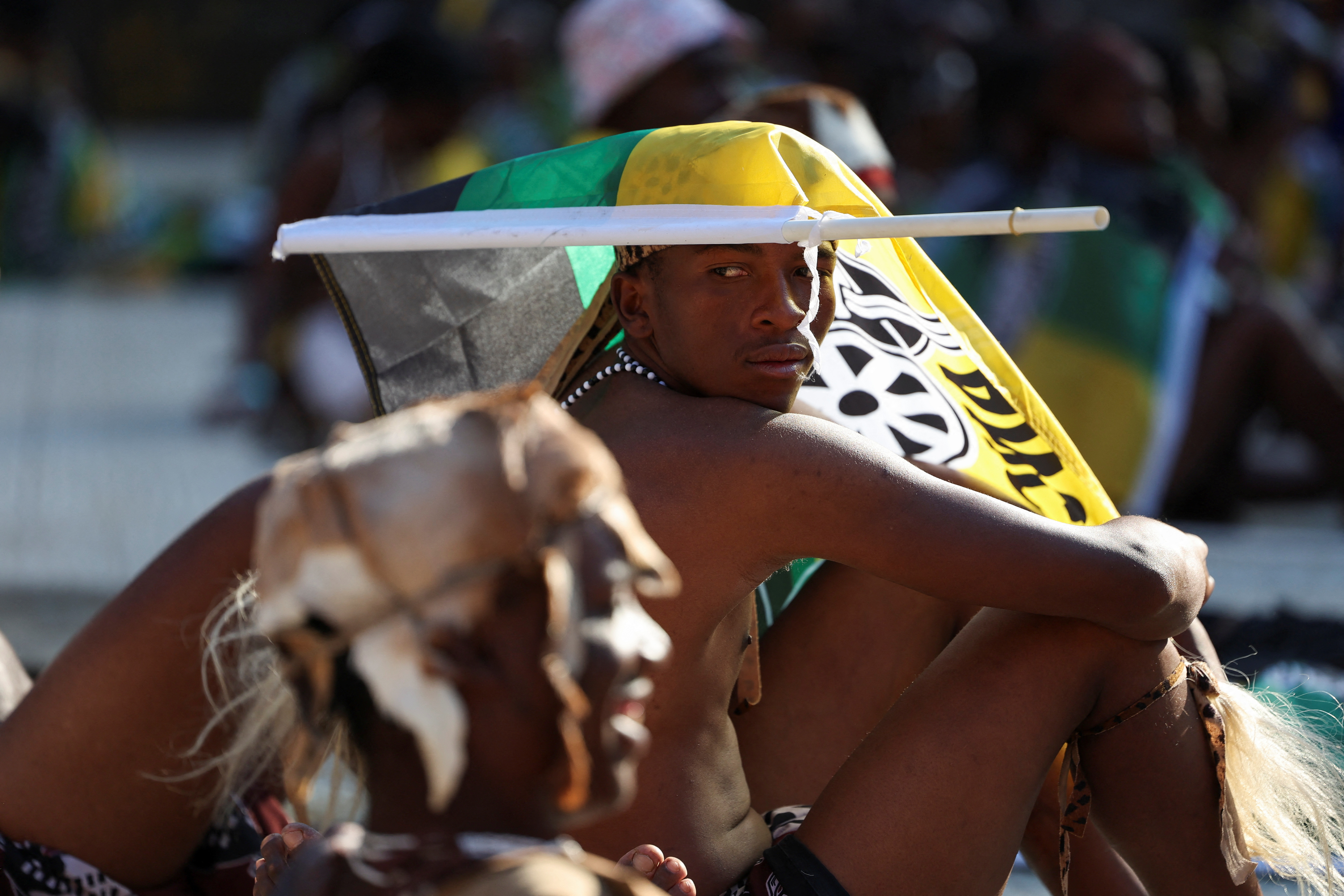 A supporter sits under the flag of the African National Congress (ANC) as South African president Cyril Ramaphosa (not pictured) speaks during the party's final rally ahead of the upcoming elections at the FNB Stadium in Johannesburg, South Africa May 25, 2024. REUTERS/James Oatway