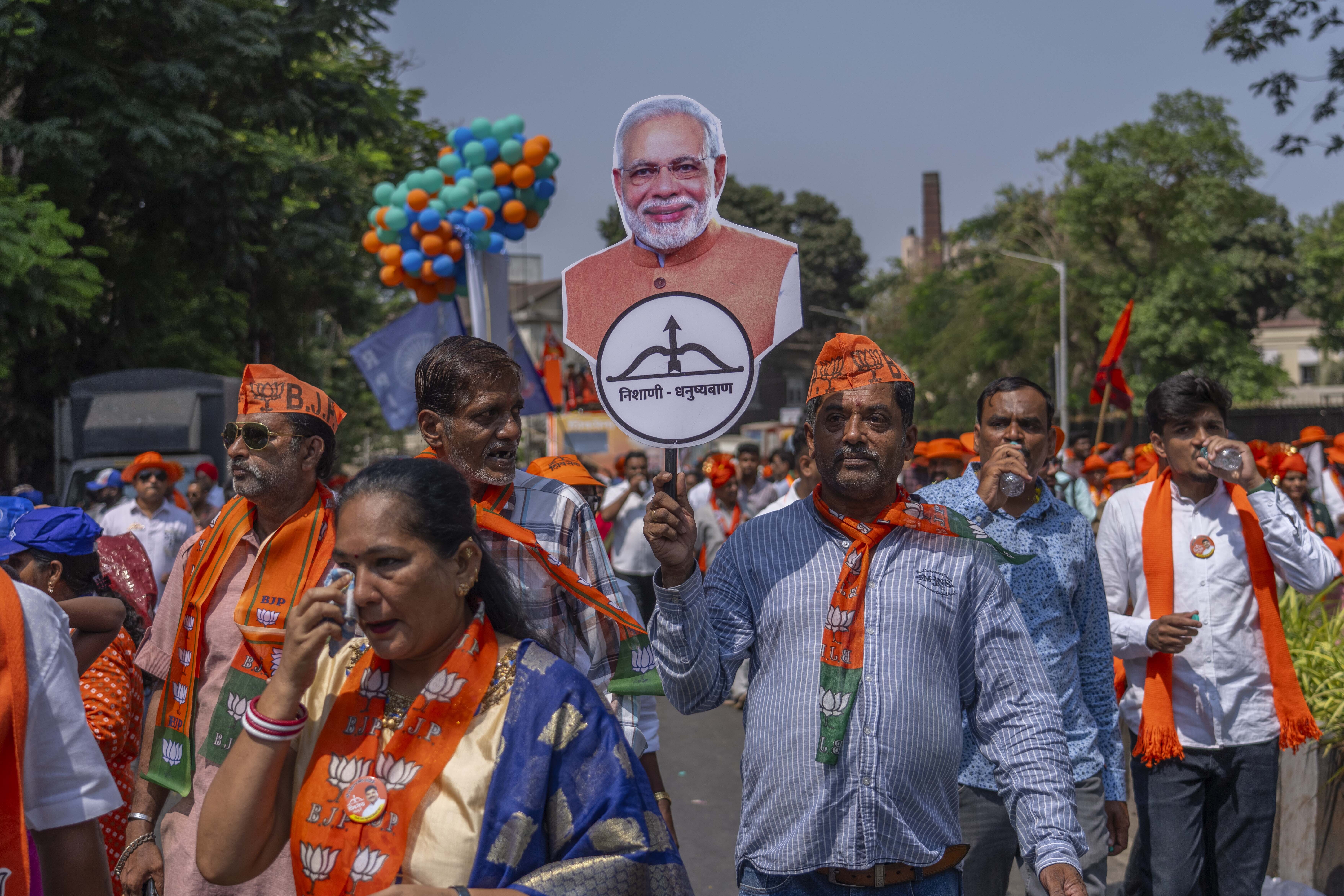 Supporters of National Democratic Alliance walk in a road show as one of them holds a cutout photo of Indian Prime Minister Narendra Modi as their candidates arrive to file nomination papers ahead of national elections in Mumbai, India, Monday, April 29, 2024. (AP Photo/Rafiq Maqbool)