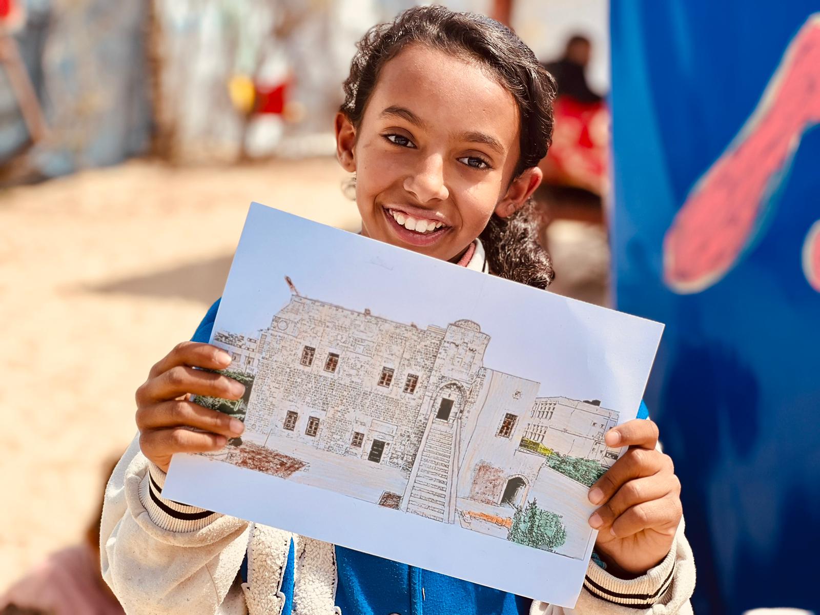 Amal (not her real name), 11, beams as she displays her artwork of Qasr Al-Basha during a children’s workshop in Rafah, Gaza, designed to keep Palestinian cultural heritage alive despite the war.