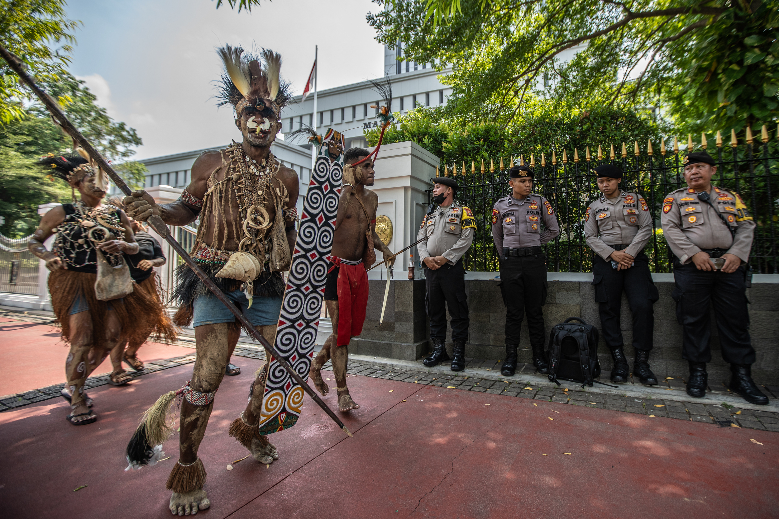 Indigenous people from Papua in traditional clothing. There is a row of Indonesian policeman leaning on the railings of the Supreme Court.