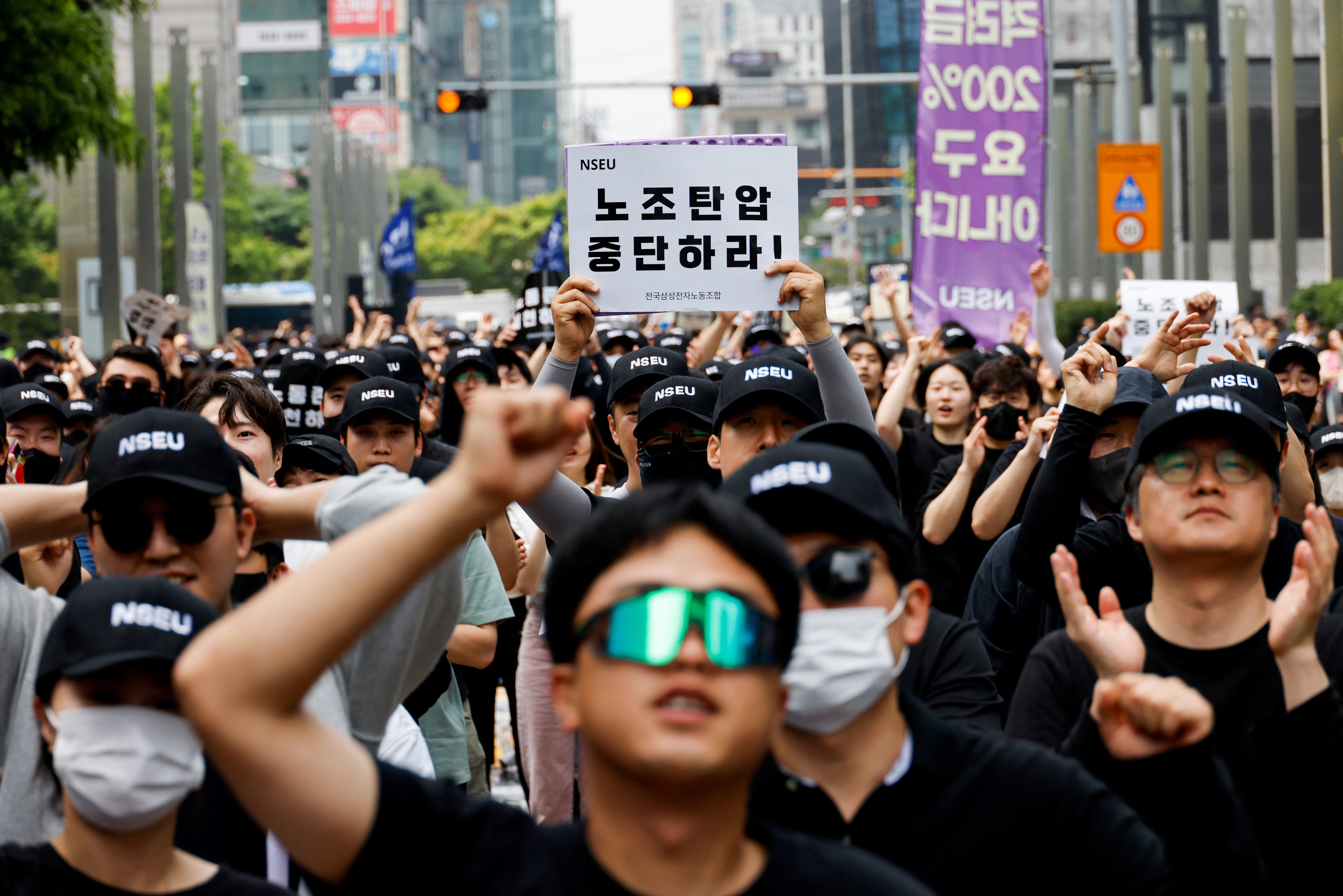 Members of the Electronics Union (NSEU) marching in Seoul. They are holding banners that say 'Stop Union Busting'. They are wearing black. Some are punching the air