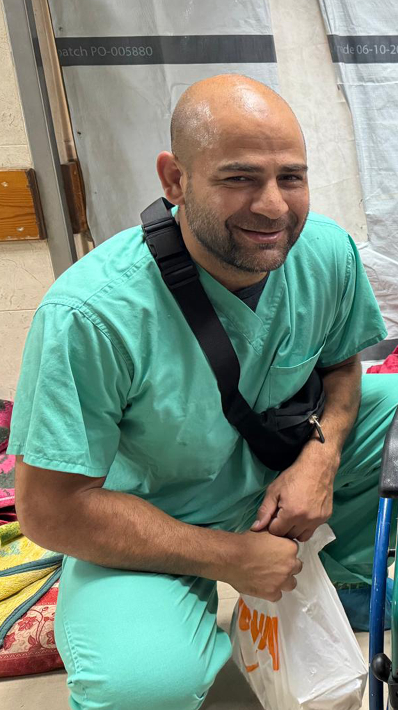 Omar Sabha kneels in teal scrubs next to a young girl in a wheelchair.